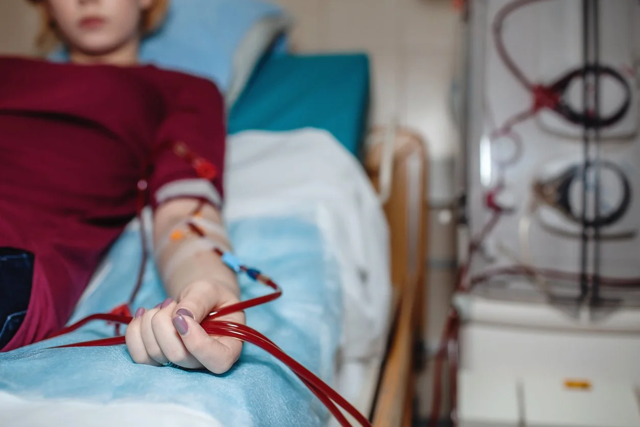 A person lying in a hospital bed donating blood, with a needle and tubing connected to their arm.