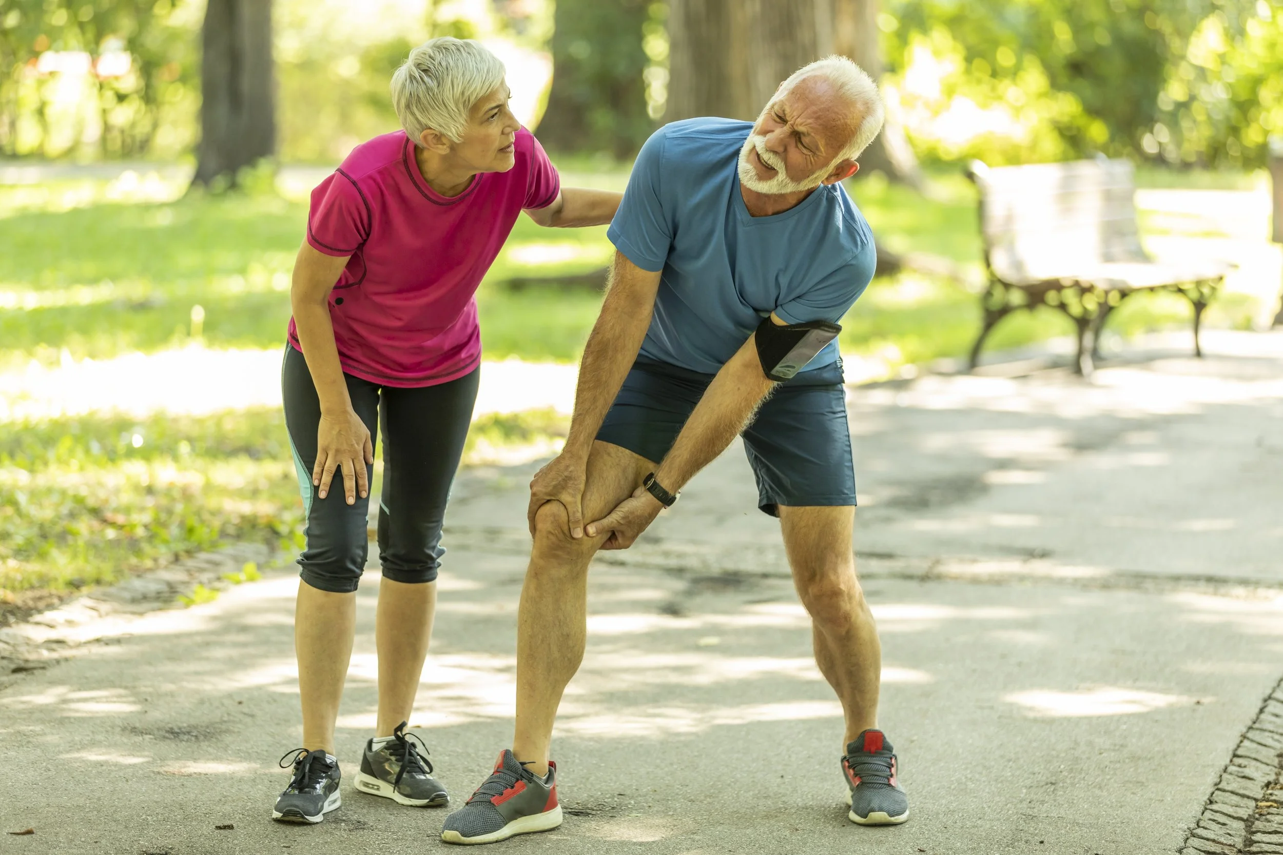 An elderly man with a knee injury receiving assistance from a woman in a park.