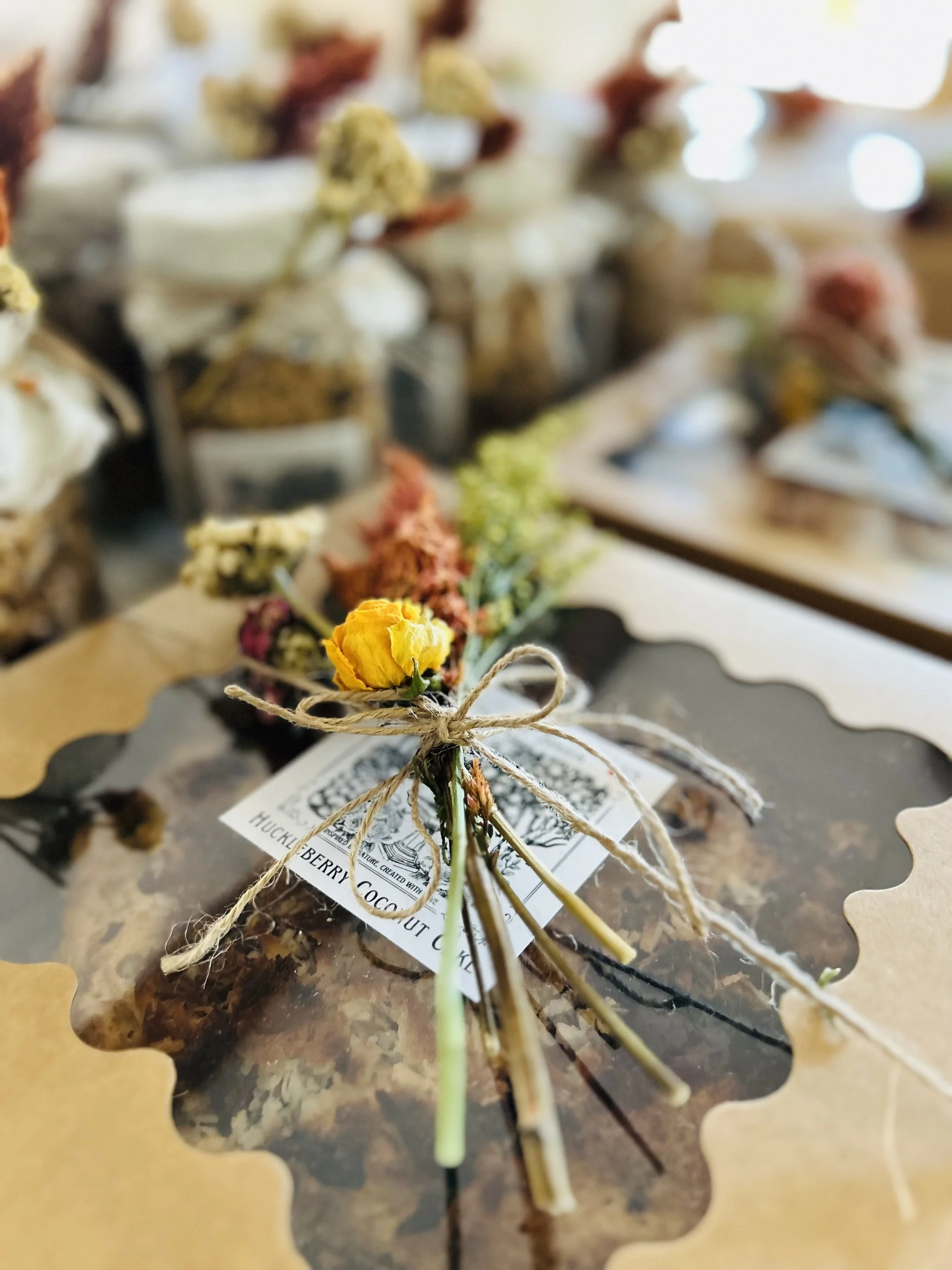 A bouquet of dried flowers tied with twine, placed on top of a chocolate cake with a decorative cut-out border, displayed in a bakery or cafe setting.