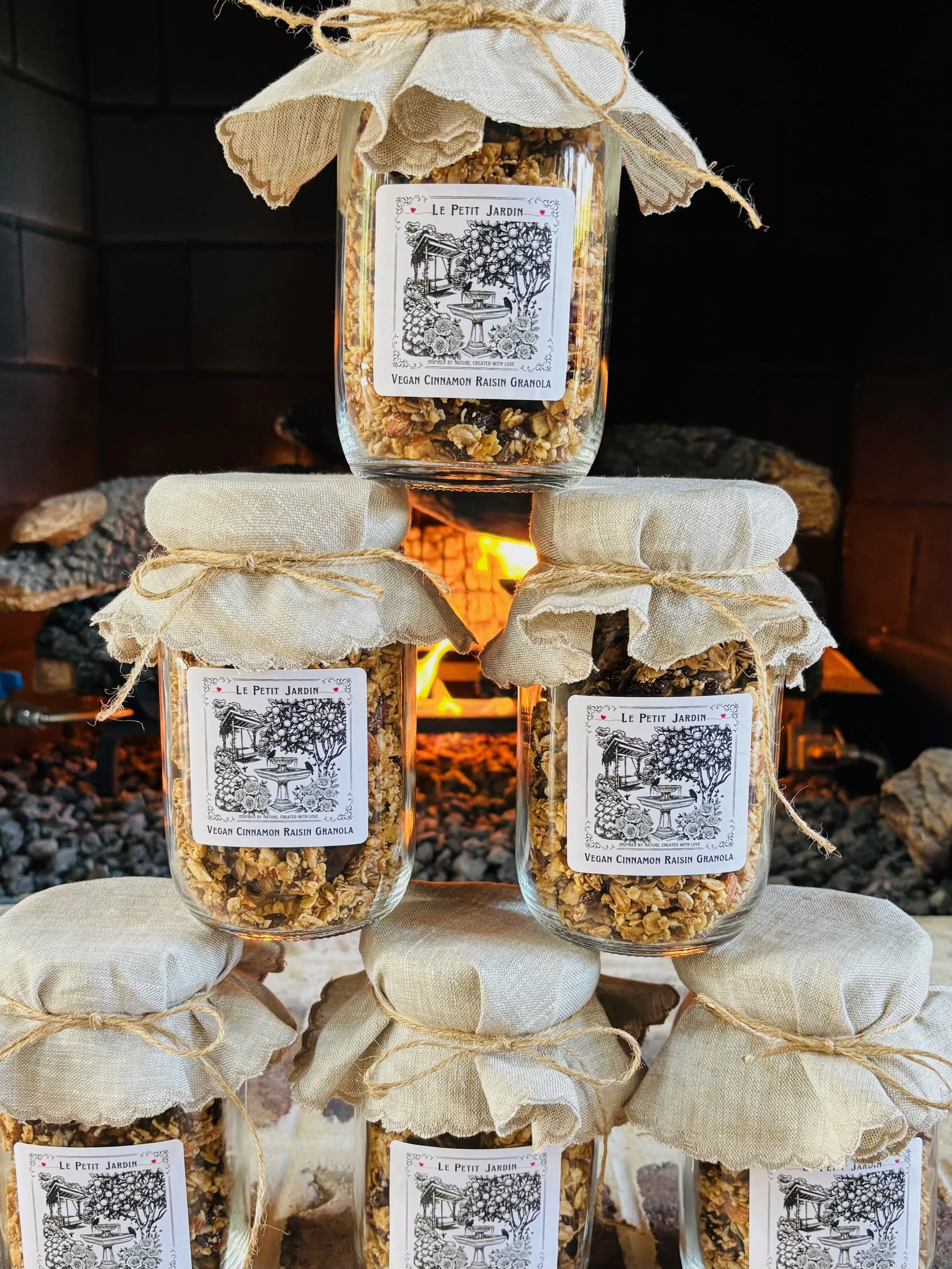 Stacked jars of vegan cinnamon raisin granola with fabric covers and twine, in front of a fireplace