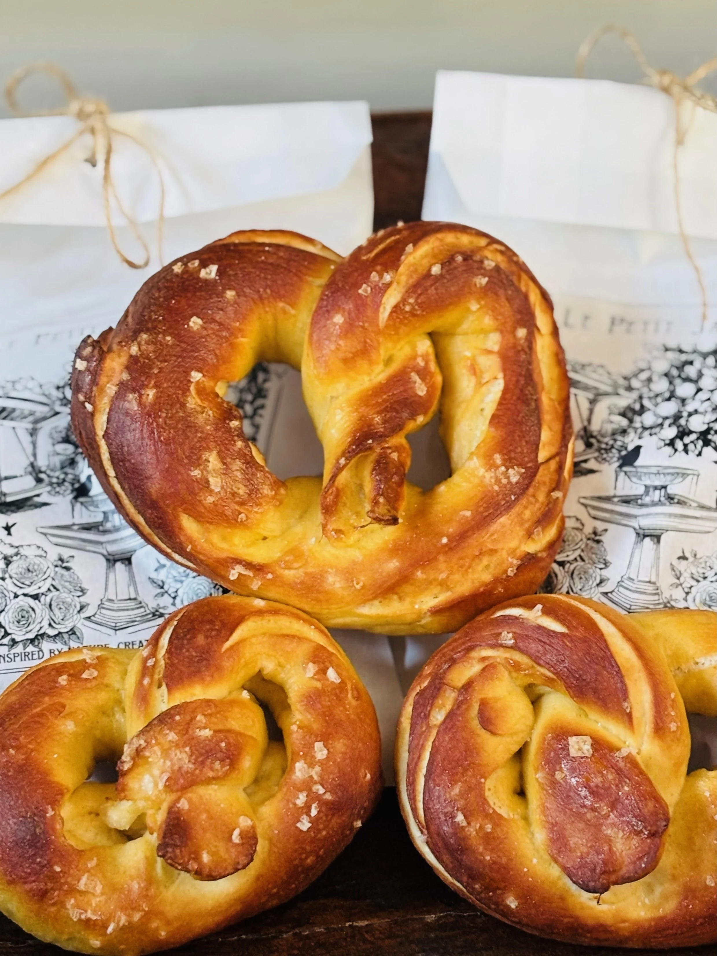 Three freshly baked pretzels with coarse salt on top, arranged on a black tray with a decorative paper underneath.