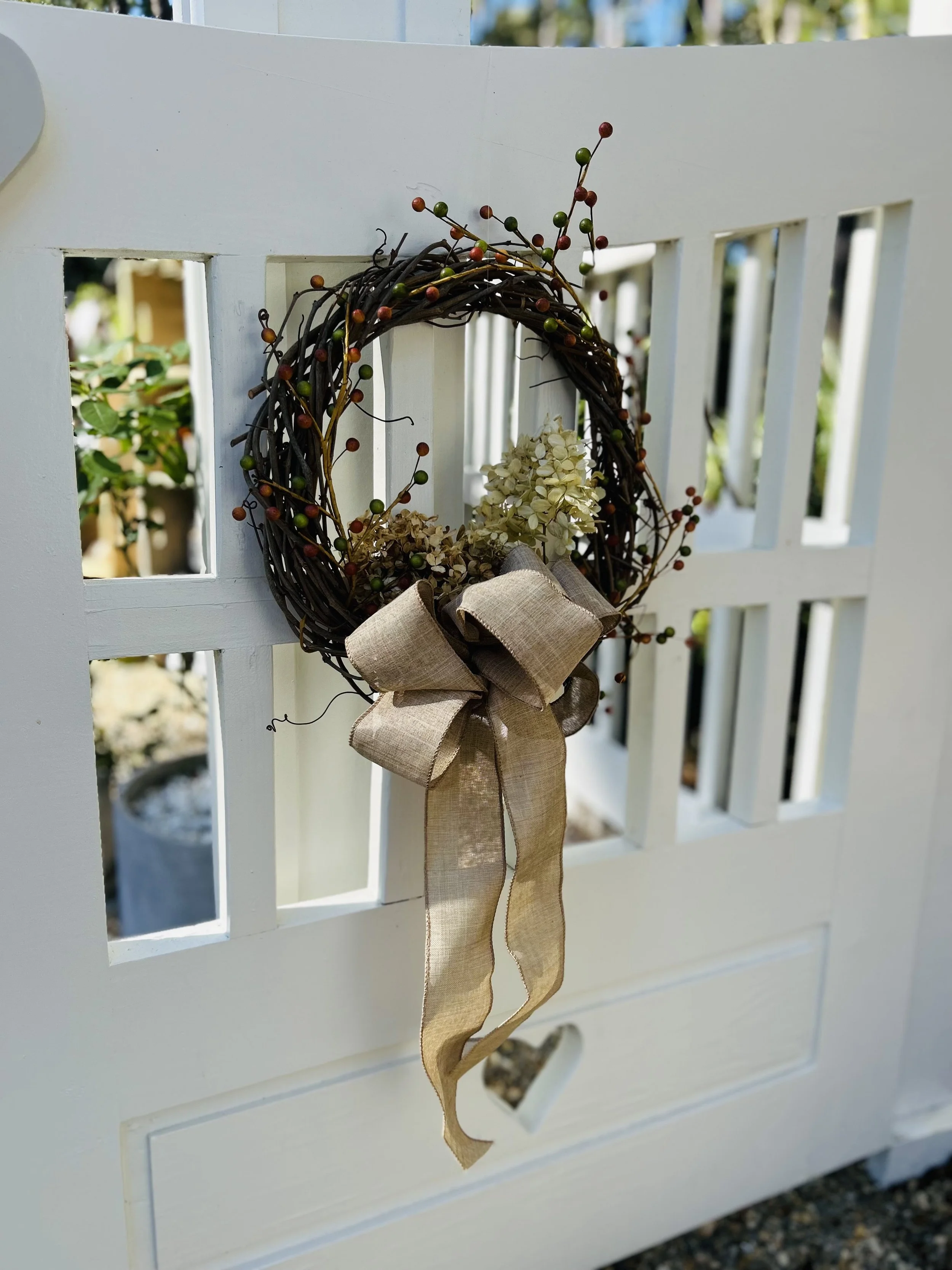 Decorative wreath with a beige bow hanging on a white gate.