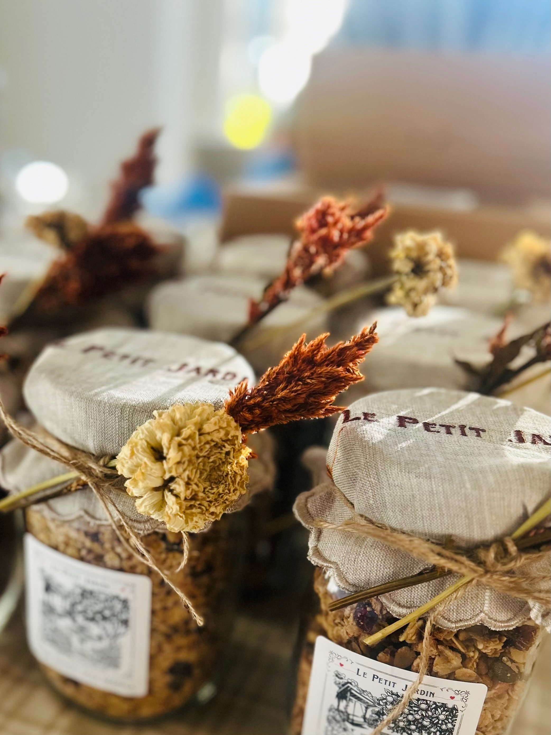 Collection of glass jars filled with granola, decorated with fabric lids, twine, and dried flowers.