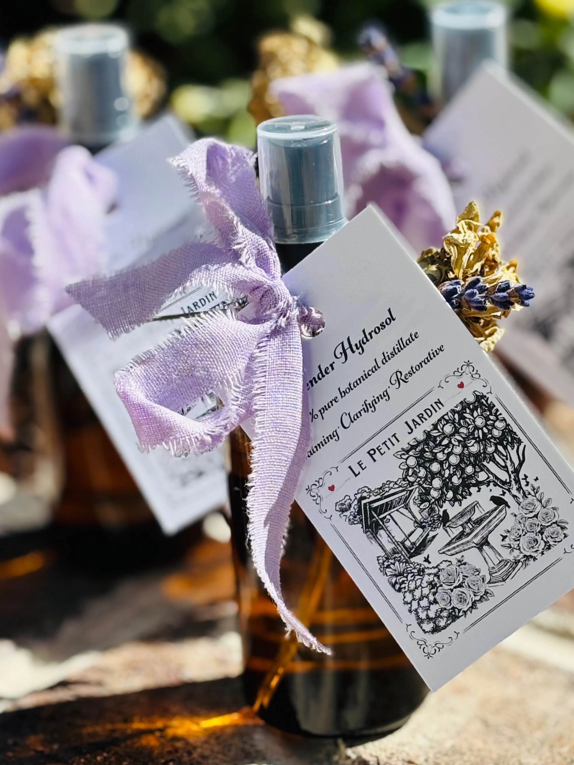 Small brown bottle labeled 'Lavender Hydrosol' with a purple ribbon tied around its neck and a white tag attached, placed on a wooden surface with blurred background.