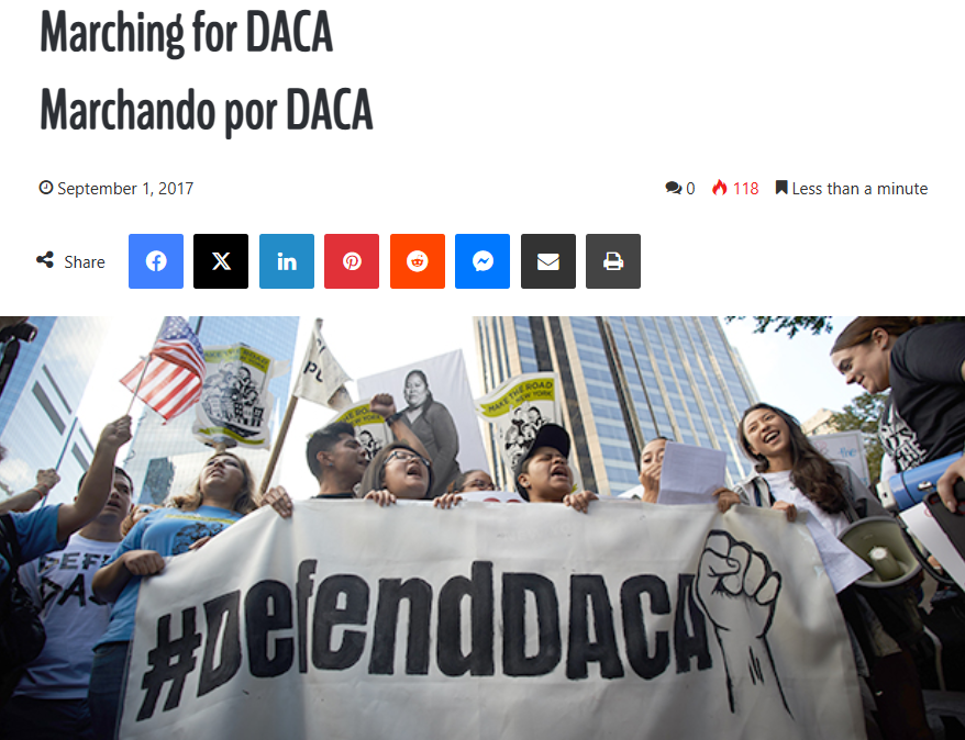 Protesters holding signs and banners during a rally for DACA, with some flags including the American flag. The banner prominently displays '#duendDACA' with a raised fist symbol.
