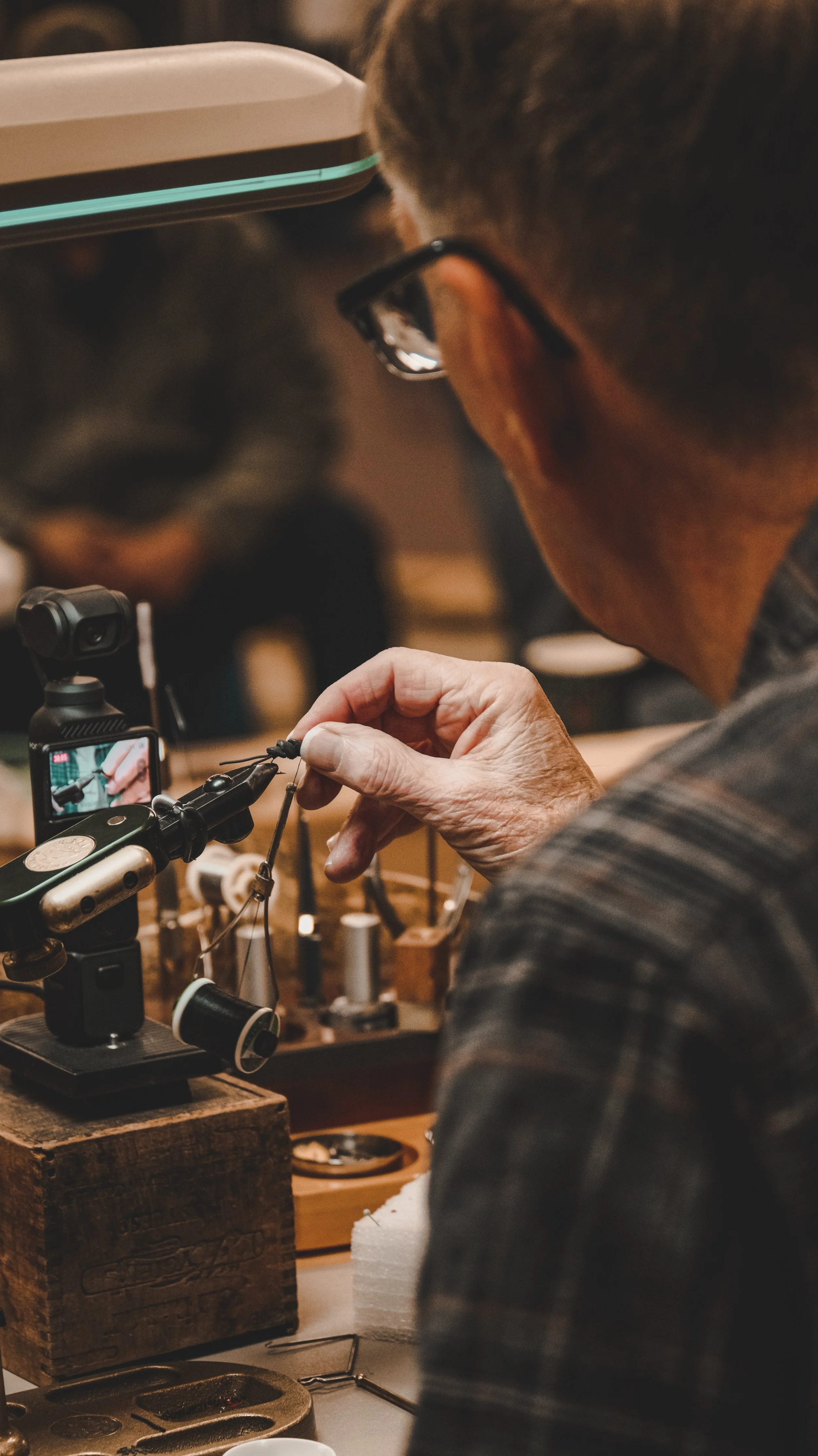 A person working on a craft project, possibly jewelry, with various tools and materials on a wooden workspace.