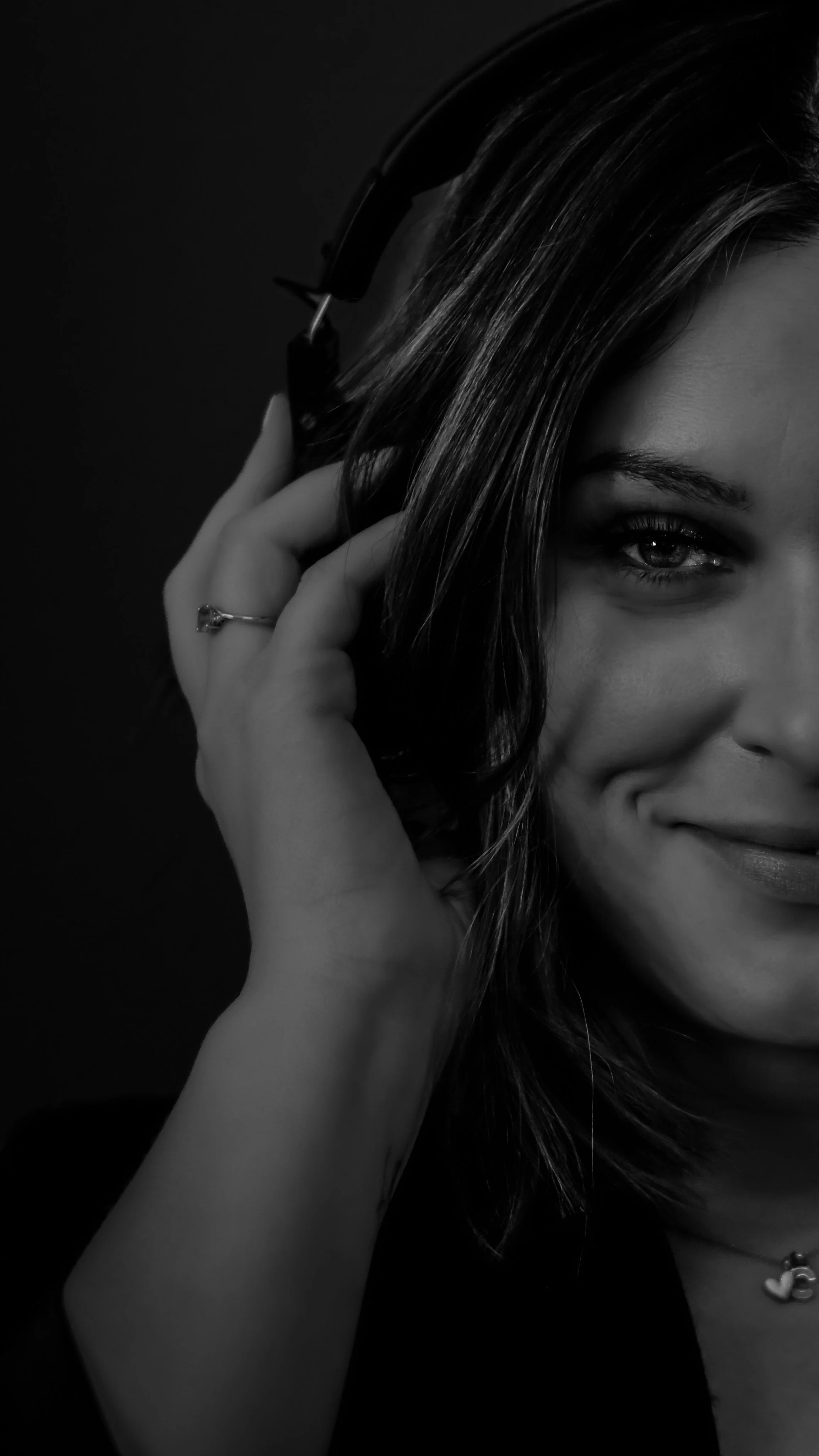 A beige speckled ceramic vase with a narrow neck, holding dried brown seed pods and plant stems, placed on a wooden surface next to a textured beige wall cast by soft natural light.