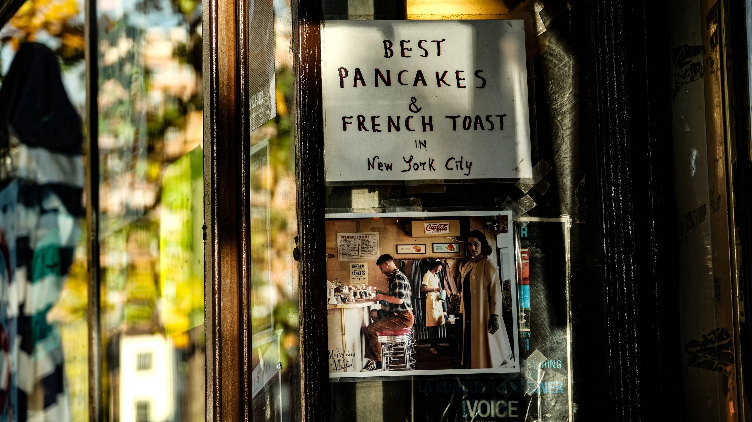 Sign advertising "Best pancakes & French toast in New York City" with a photo of the inside of a café showing customers at a counter and a waiter in the background.