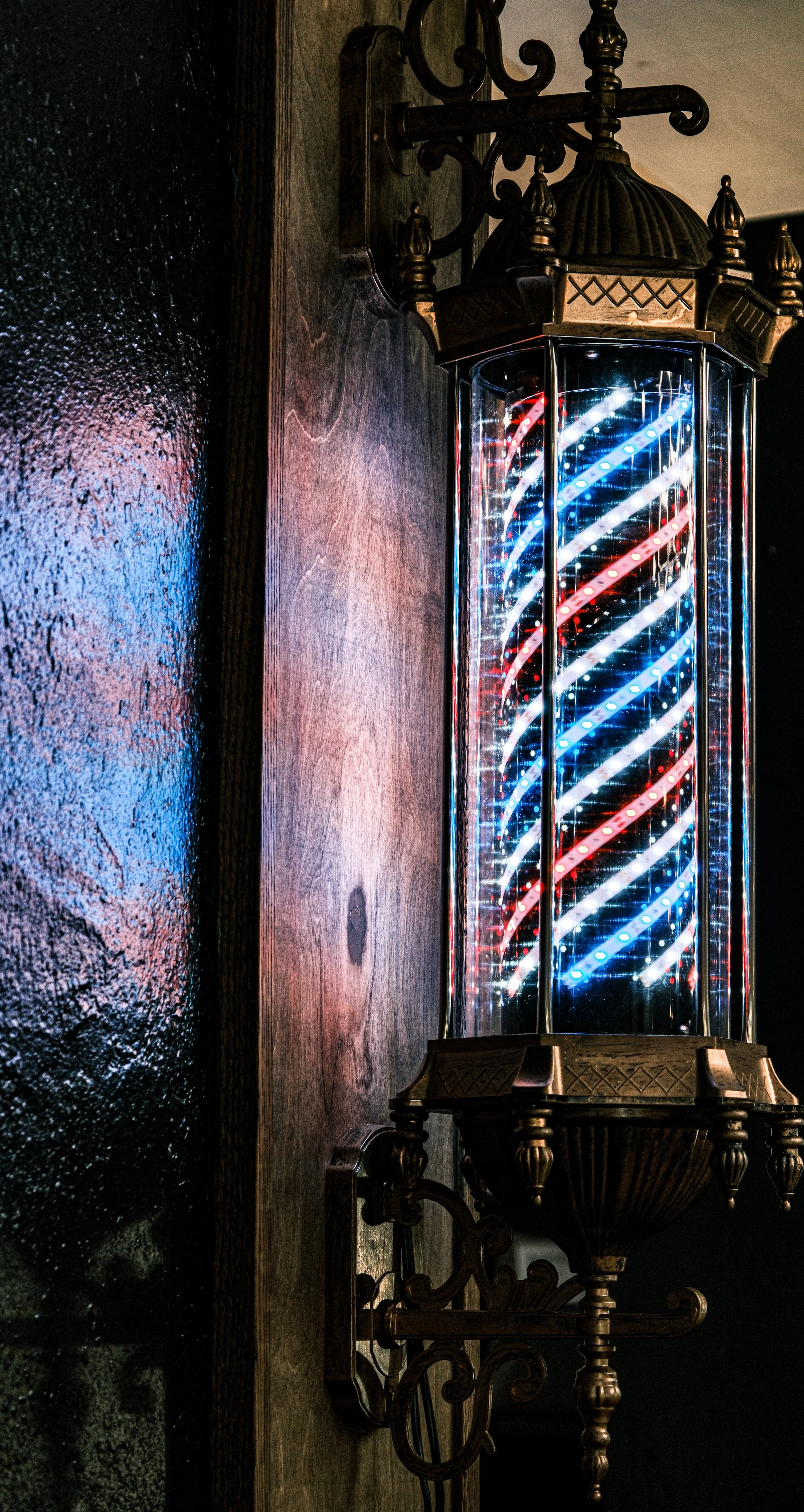 Wall-mounted vintage barber pole with red, white, and blue neon lights.