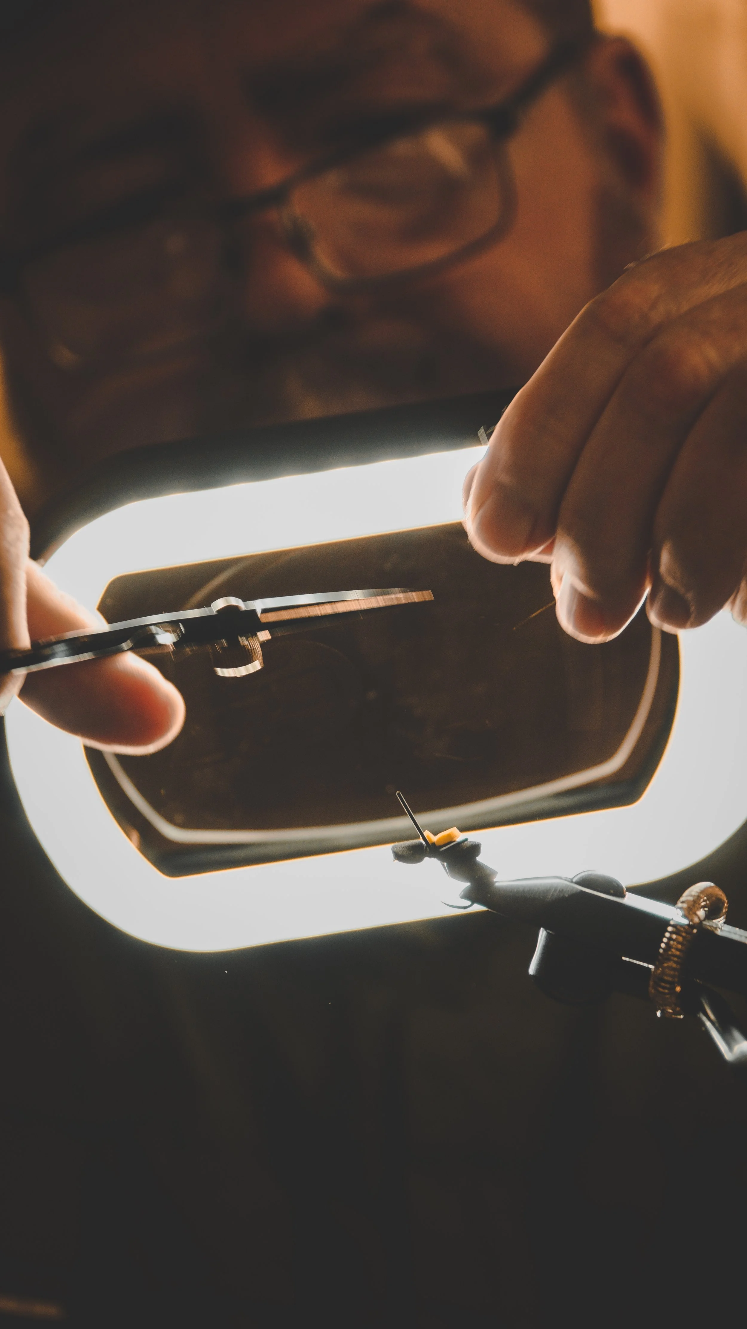 An individual assembling a guitar pickguard near a bright light, with various tools and screws visible.