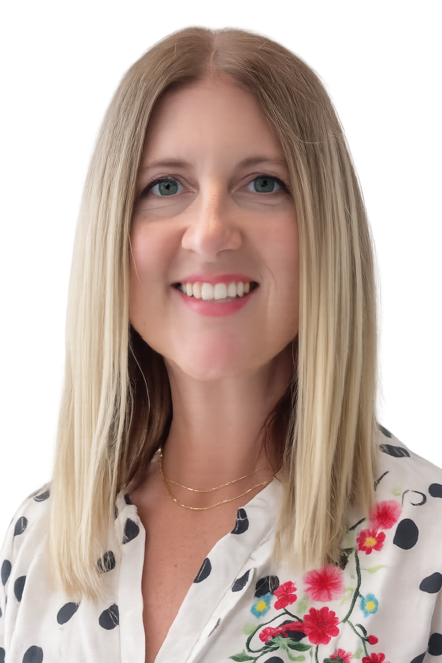 A woman with shoulder-length blonde hair, blue eyes, and a friendly smile, wearing a white blouse with black polka dots and colorful embroidery, and gold layered necklaces.