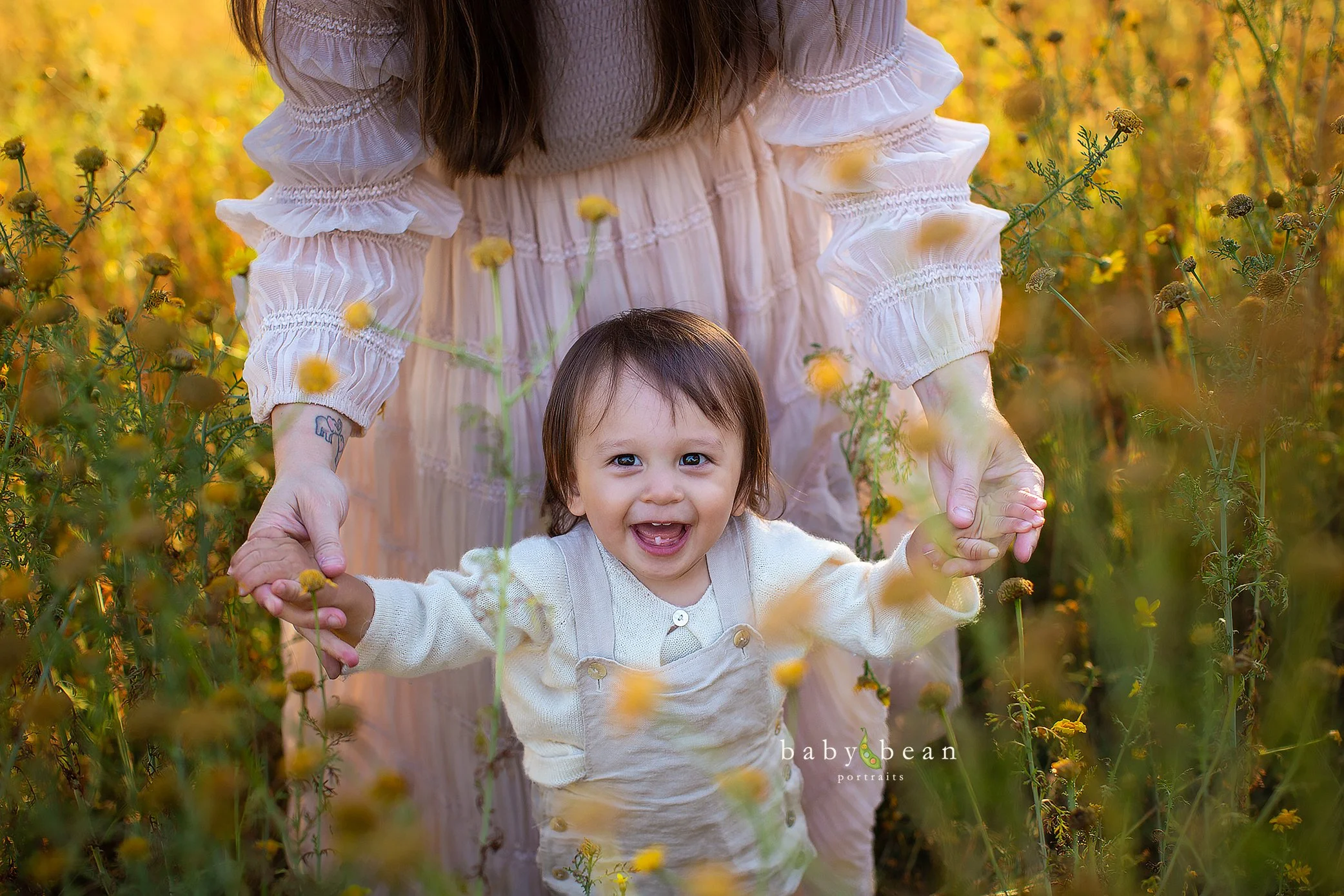 A woman and a young girl holding hands in a field of yellow flowers during sunset, smiling and enjoying nature.