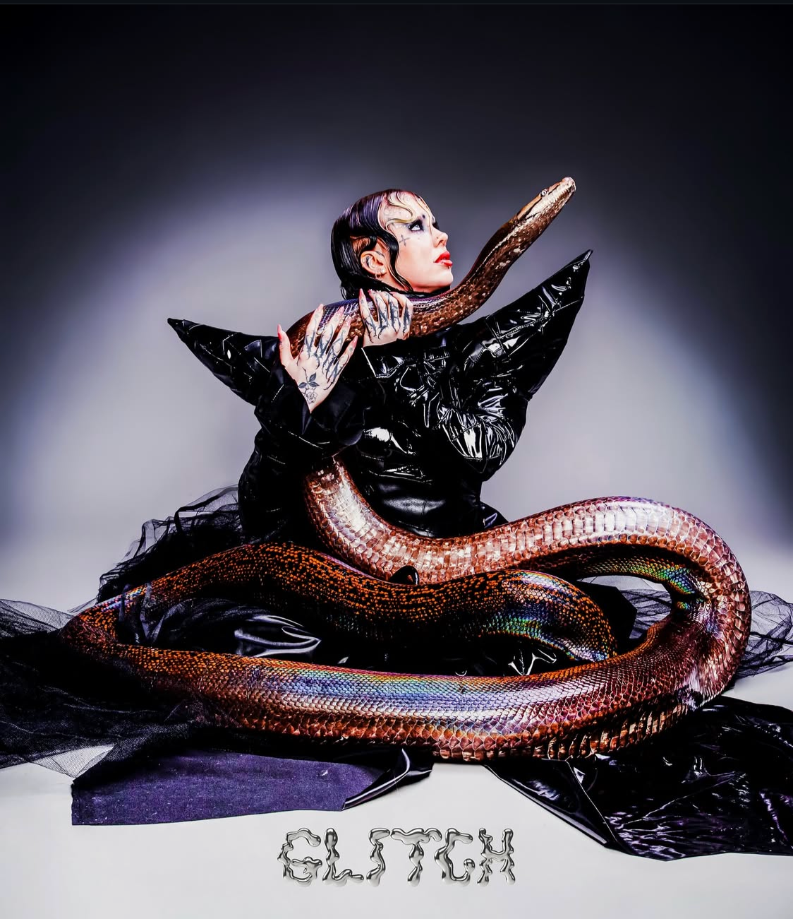 Avant-garde fashion editorial for GLITCH-MAGAZINE: High-shine latex garments with exaggerated shoulders and snake-handling conceptual styling.