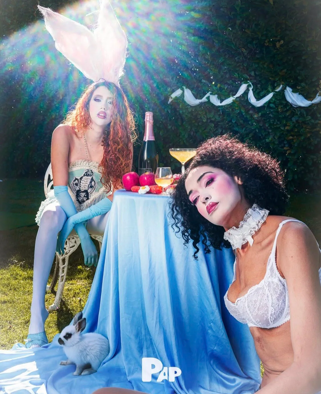 Surreal fashion editorial: Styling for a garden tea party, illustrating curly textures, blue gloves, and whimsical props in bright sunlight.