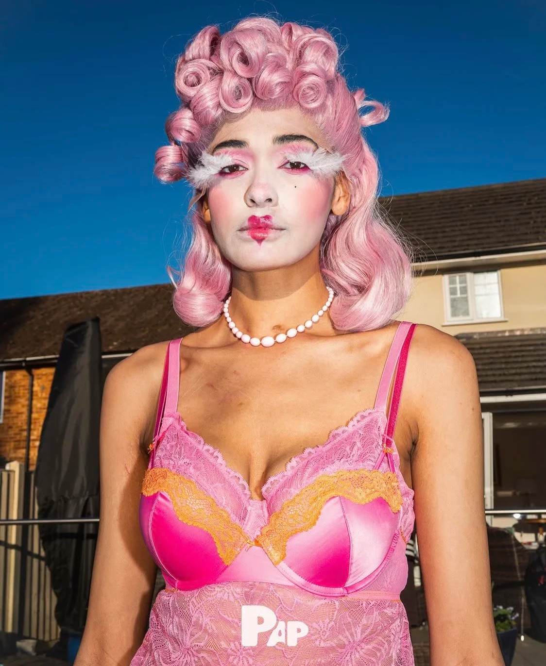 Styling portfolio: Model with vibrant pink curly hair wearing a pink lace top and a pearl necklace.