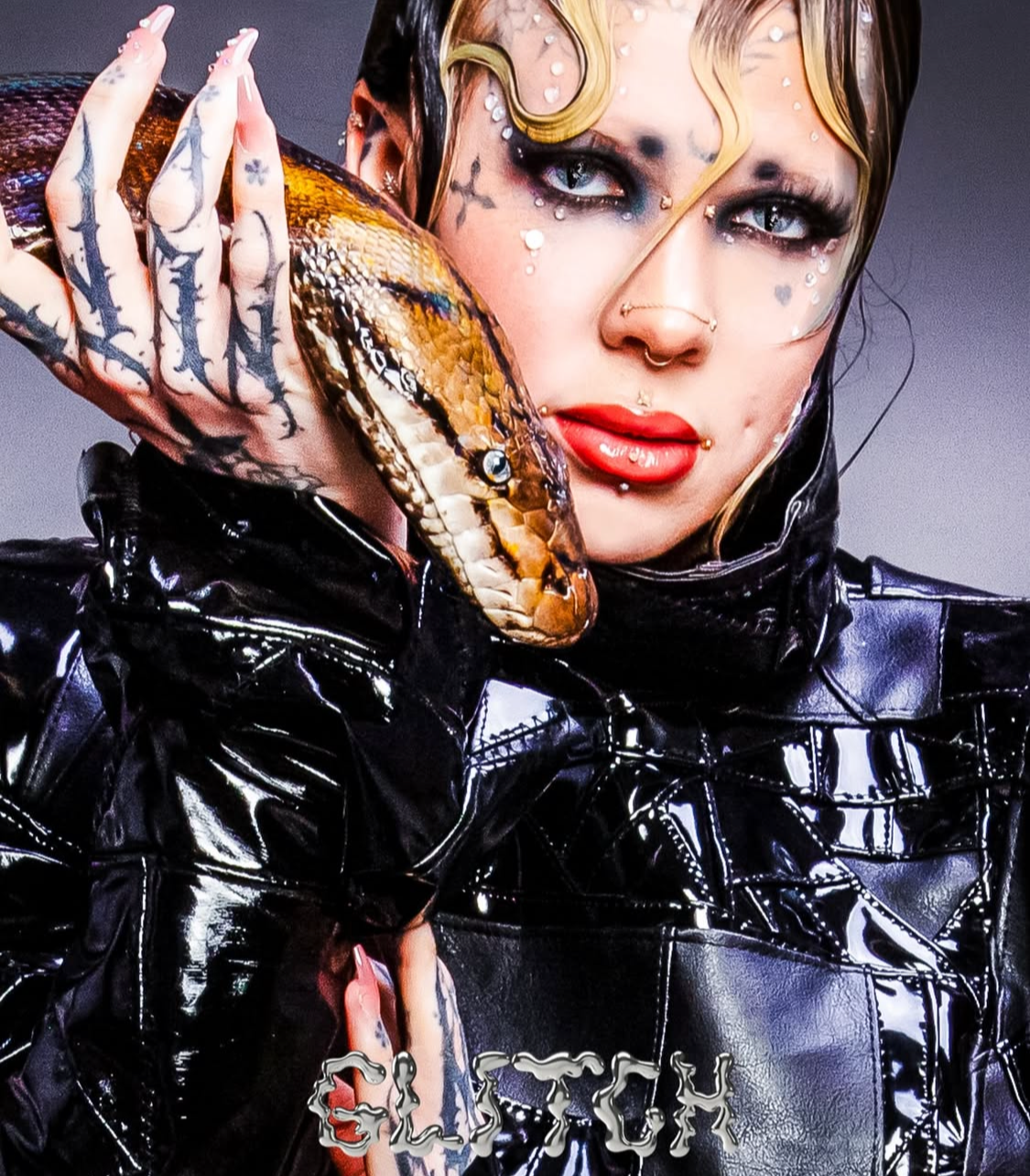 Fashion editorial styling: Model with tattoos and piercings wearing a shiny black garment and carrying a snake.