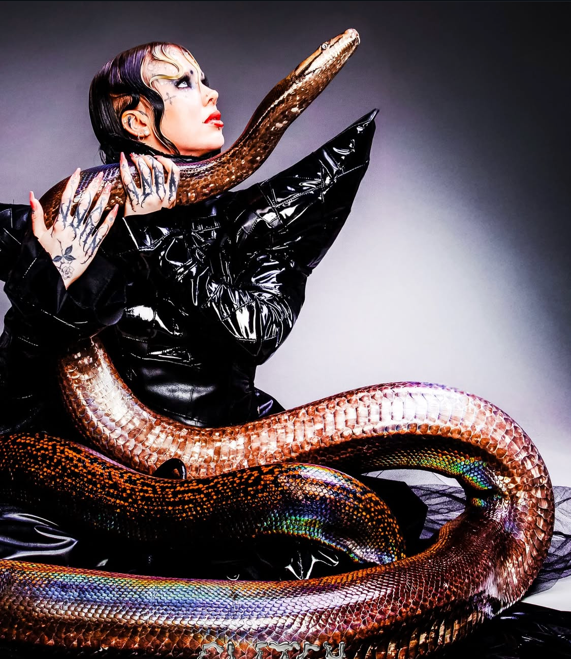 Conceptual fashion styling: Model with bold makeup in a high-shine black outfit with a snake.