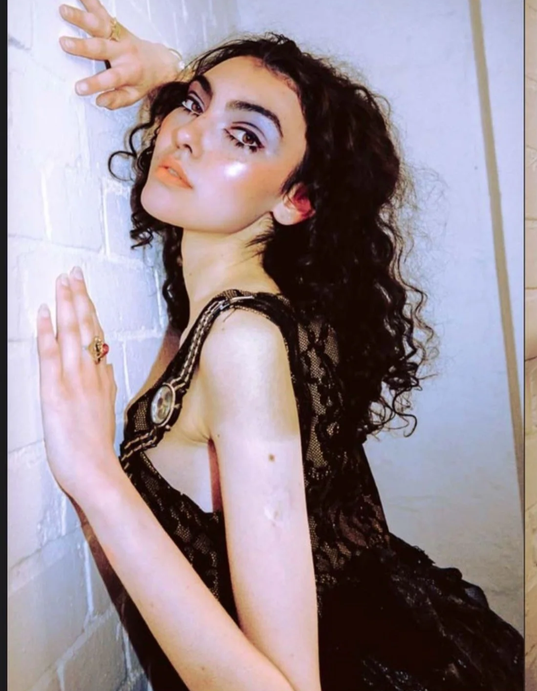 Studio styling: Intricate black lace textures and sheer layering posed against an industrial white brick backdrop.