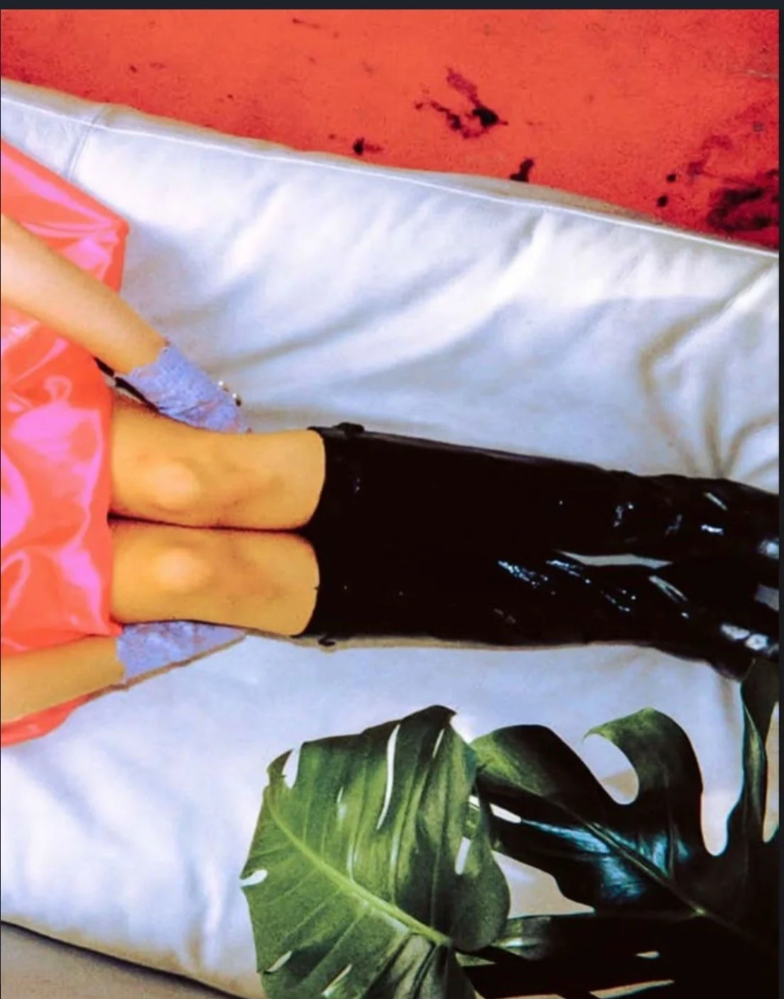 Fashion detail study: Juxtaposition of high-shine black vinyl boots against soft pink ruffles and patterned textiles.