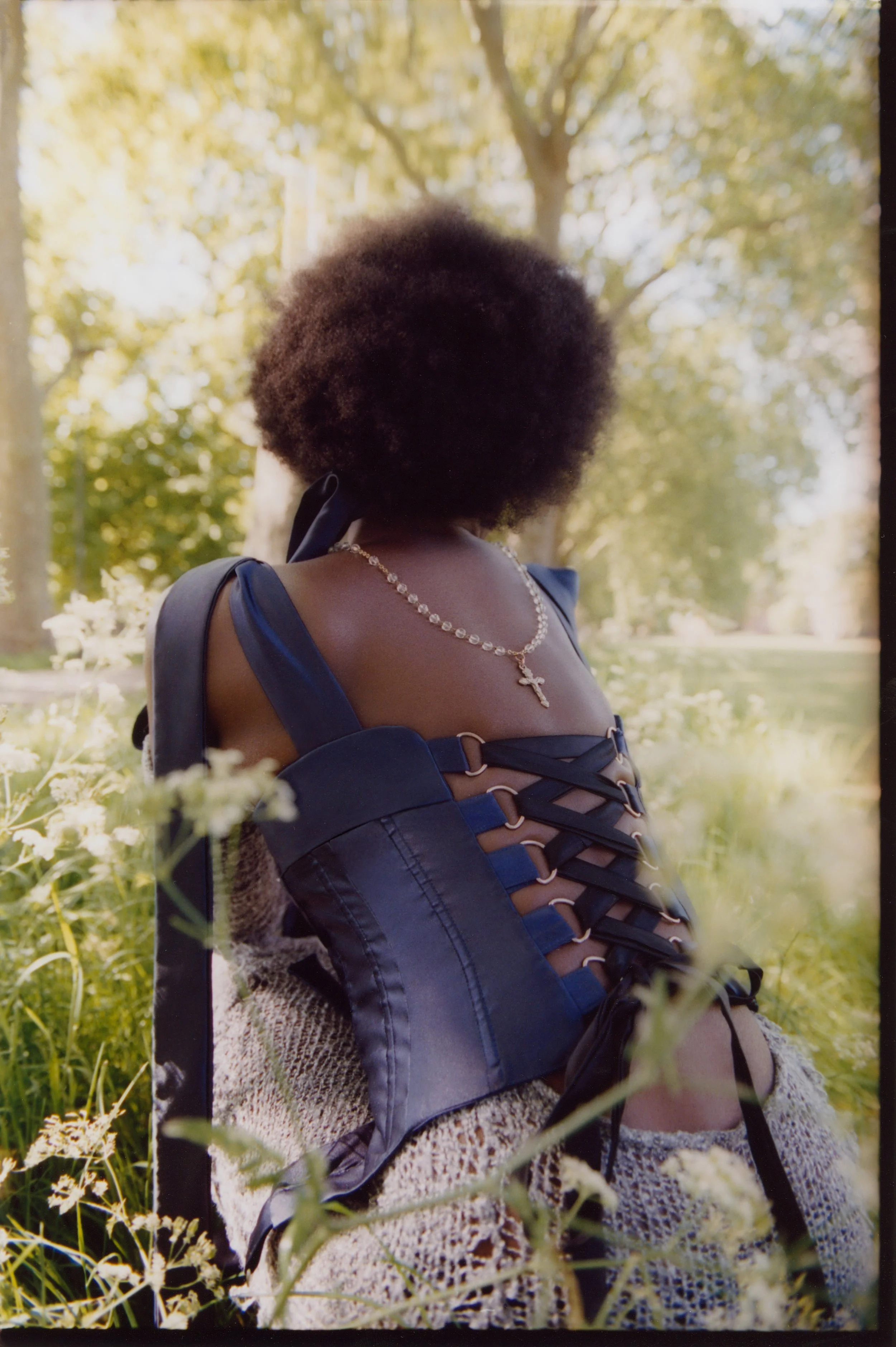 Fashion editorial featuring model Mercy: Romantic styling with a navy blue corset and silver jewelry set within a wildflower field.