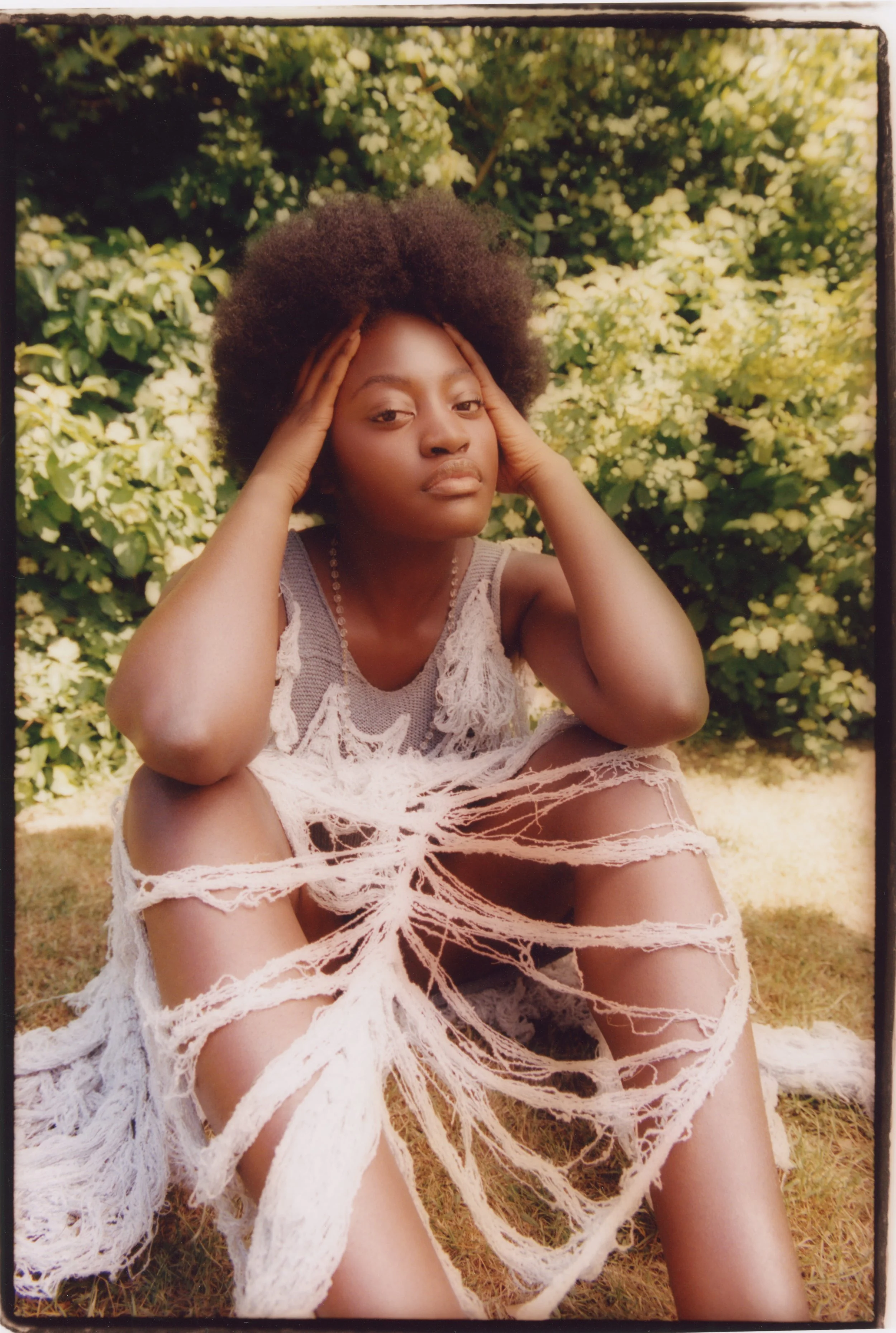 Avant-garde deconstruction: Model in a hand-distressed, oversized beige knitted dress, styled amidst structured garden shrubbery, styled by Mara Bernemann.