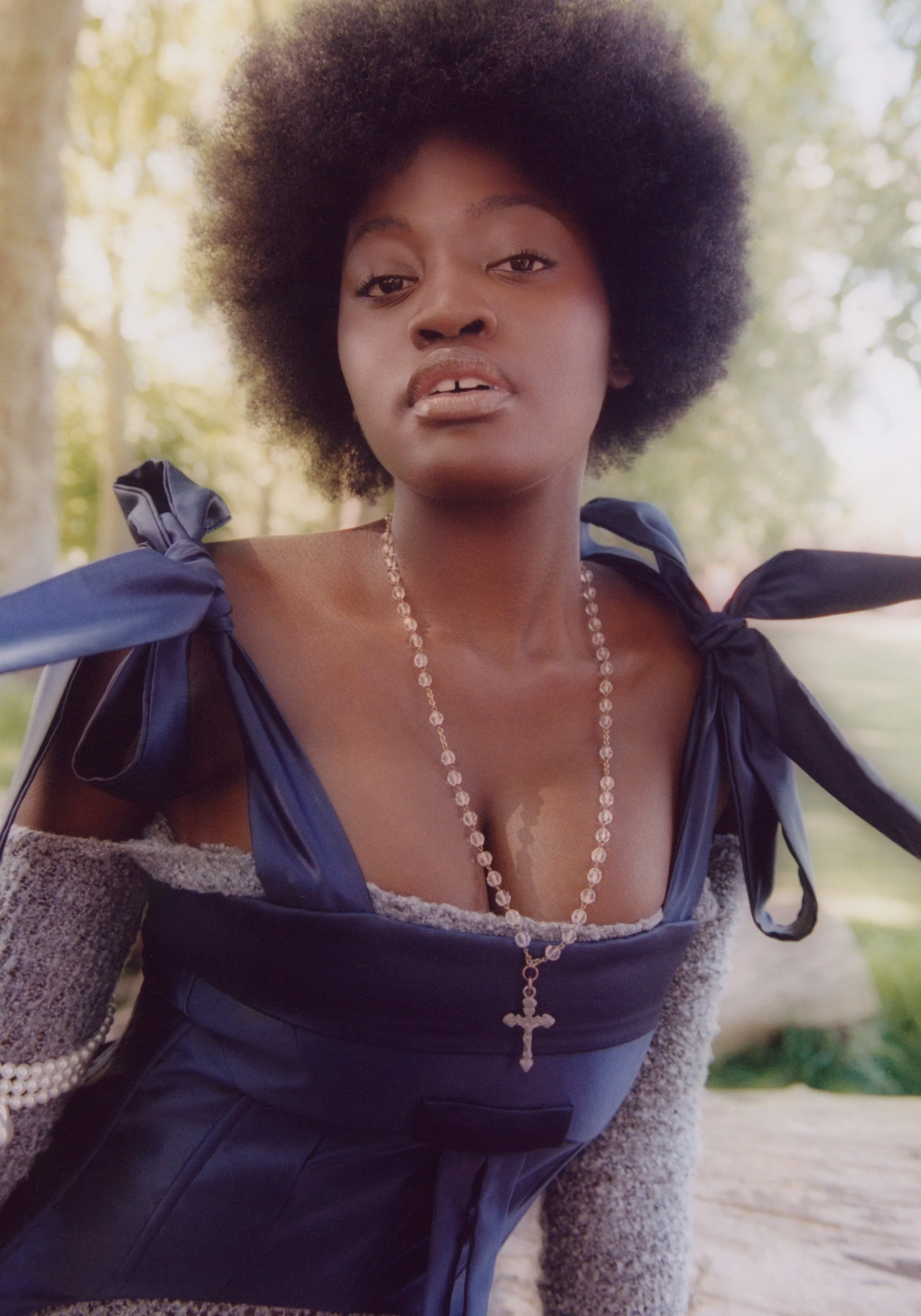 Outdoor fashion editorial: Model wearing a navy blue corset, layered textures, and a pearl cross necklace.
