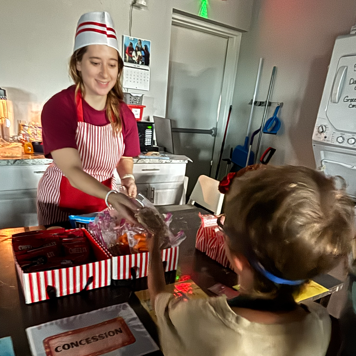 A child and adult playing pretend concession stands at a movie theater