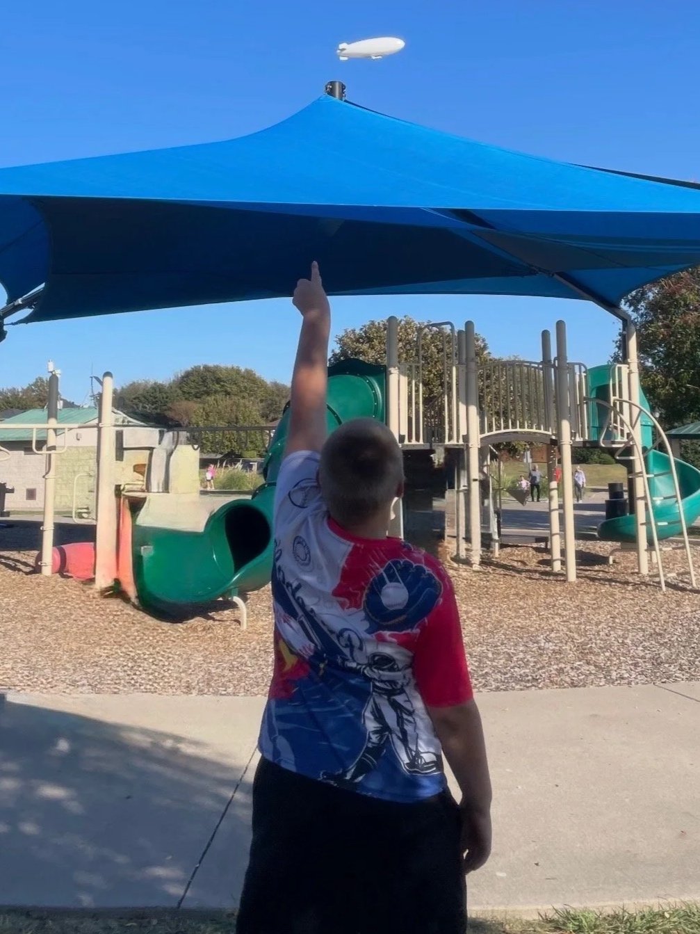 Adolescent at a park pointing toward a blimp in the sky to demonstrate observational skills