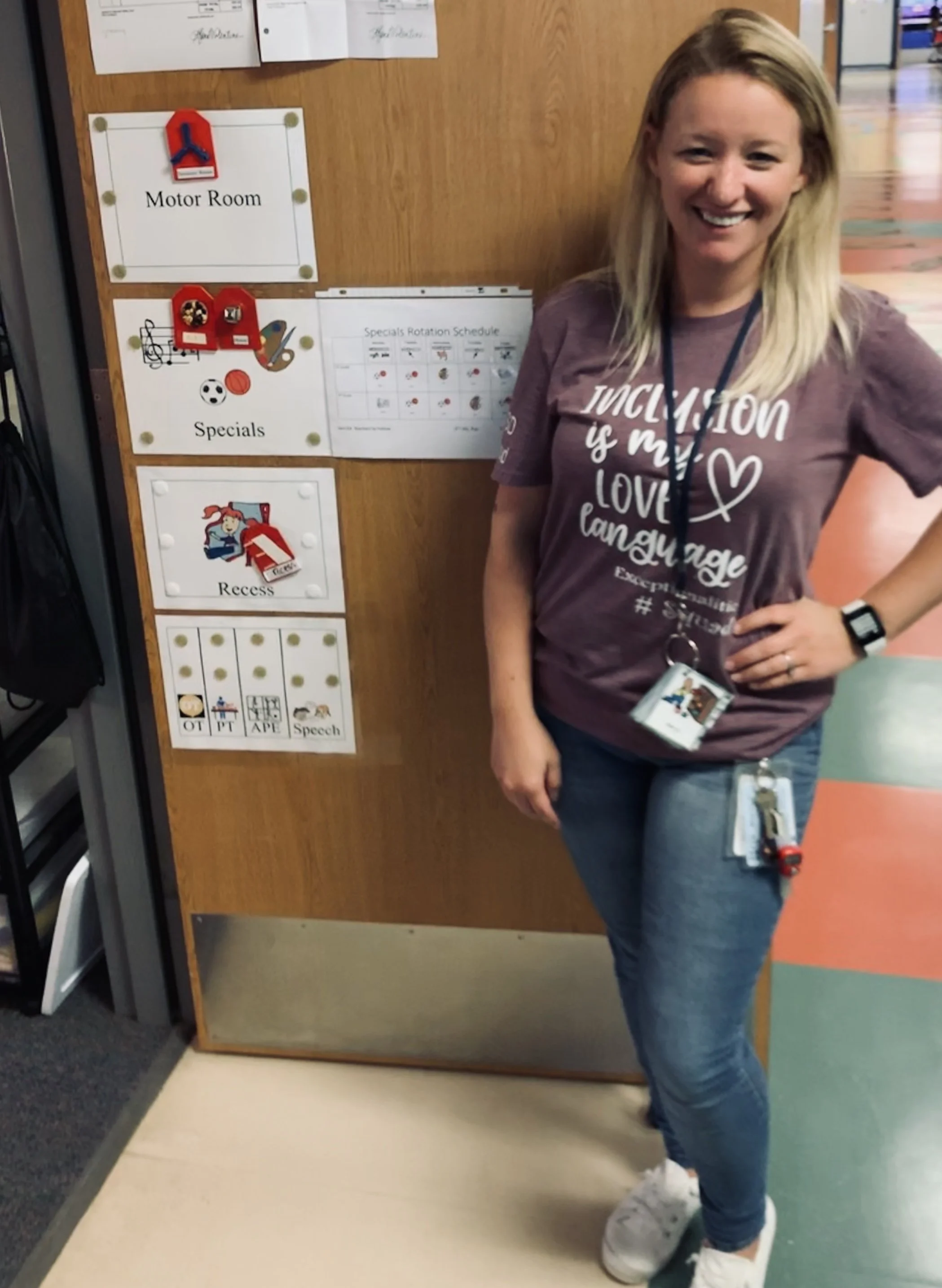 A women wearing a t-shirt saying "inclusion is my love language" standing outside of a special education classroom door