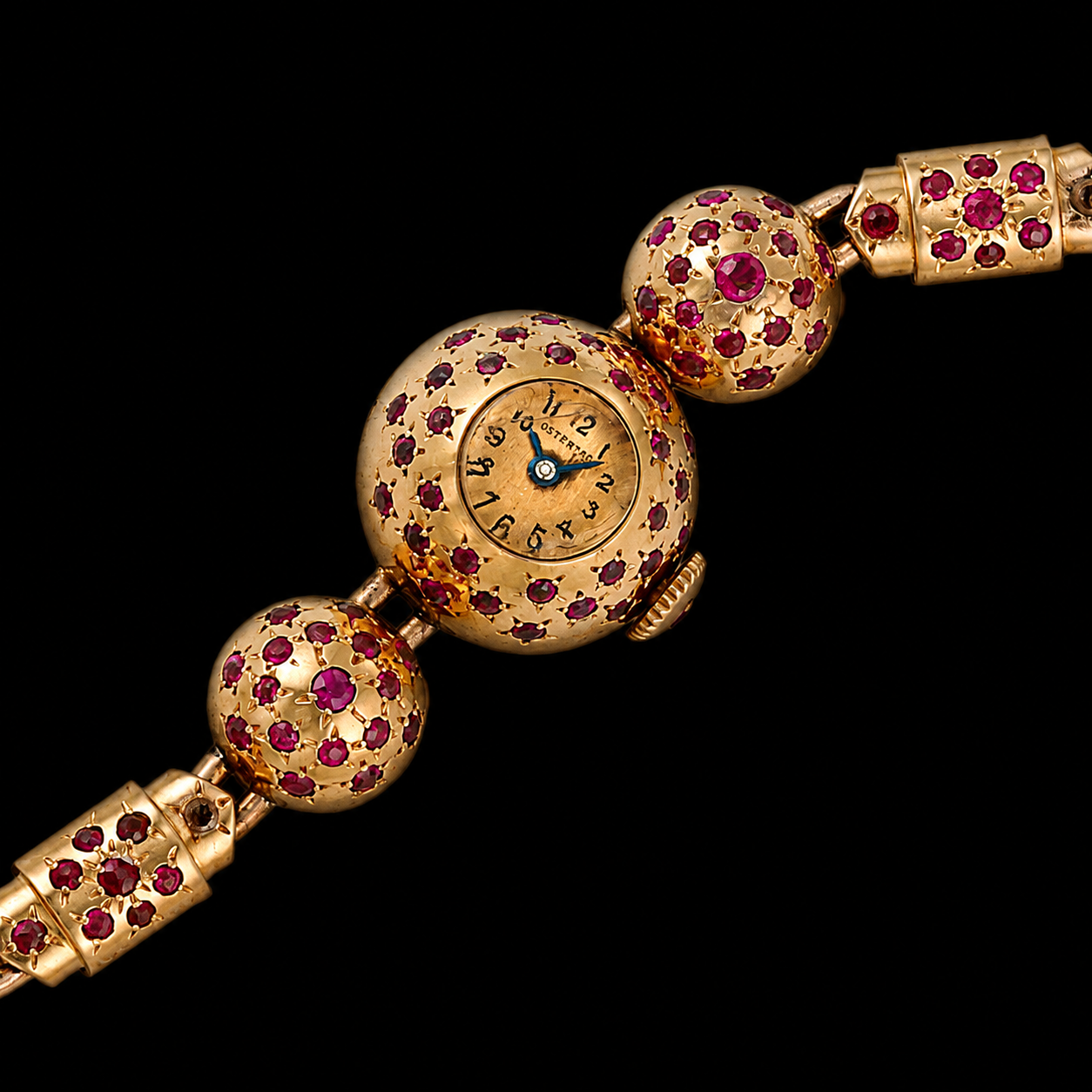 Bracelet ou montre en or fin ornée de nombreuses petites pierres précieuses rouges, avec un cadran rond avec une montre en son centre.