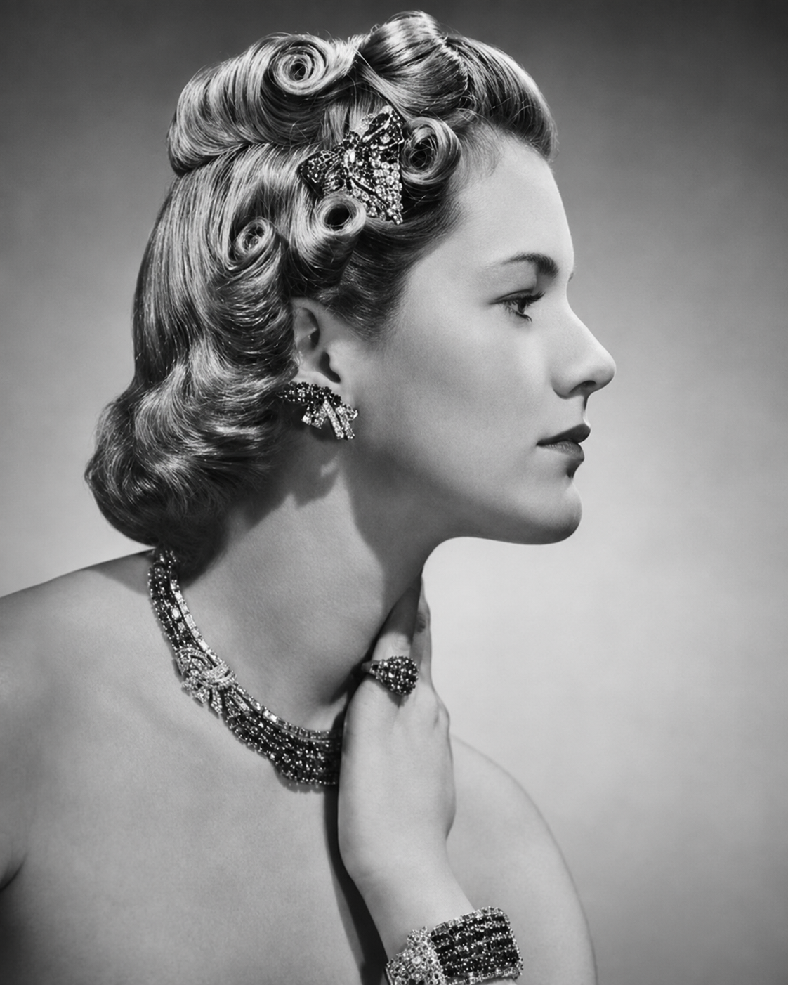 Une femme avec des cheveux bouclés et un accessoire en forme de papillon dans les cheveux, portant des bijoux étincelants, en profil, en noir et blanc.