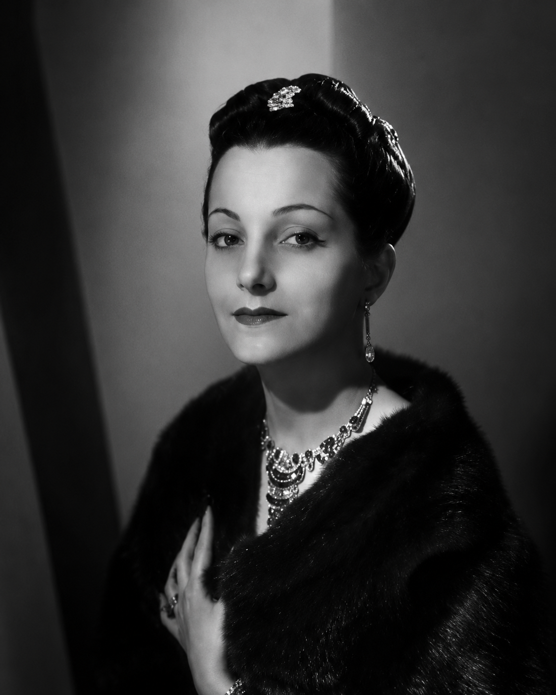 Portrait en noir et blanc d'une femme élégante portant des bijoux, un collier et des boucles d'oreilles, avec une coiffure sophistiquée et un manteau en fourrure.