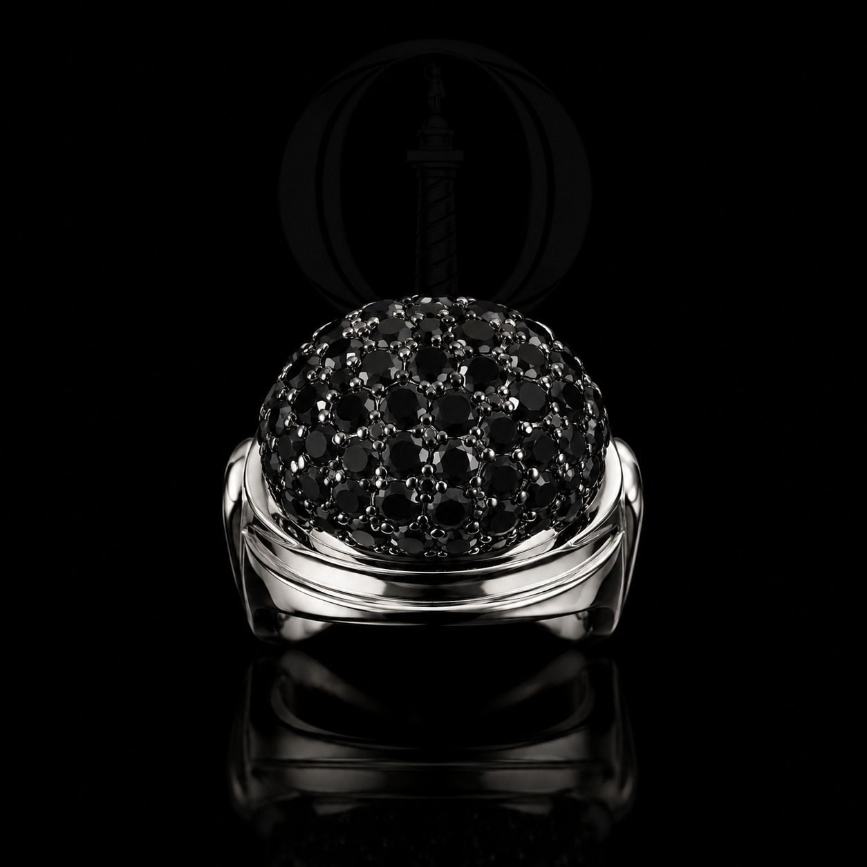 Bague en or blanc avec un globe noir orné de nombreux petits pierres noires, posée sur un fond noir avec reflet.