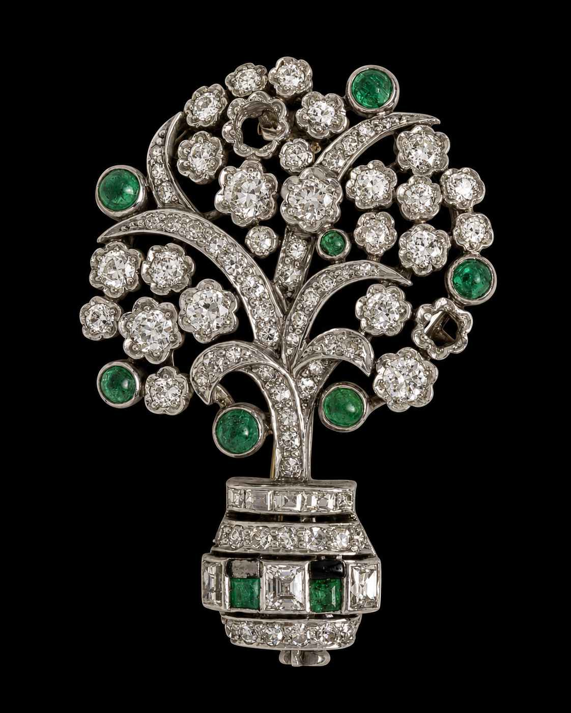 Broche en forme d'arbre avec des pierres précieuses, principalement des diamants et des émeraudes, placé sur un fond noir.