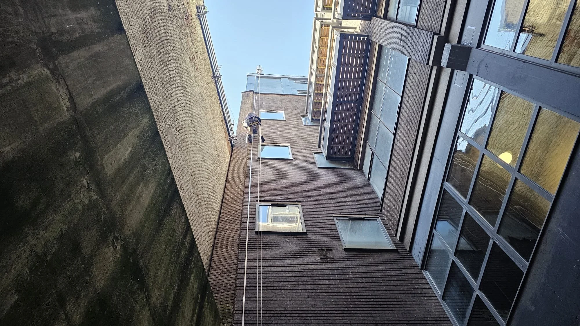 View of the interior courtyard of a multi-story building with a steeplejack on a rope, installaing lightning conductor or performing maintenance of a lightning conductor.