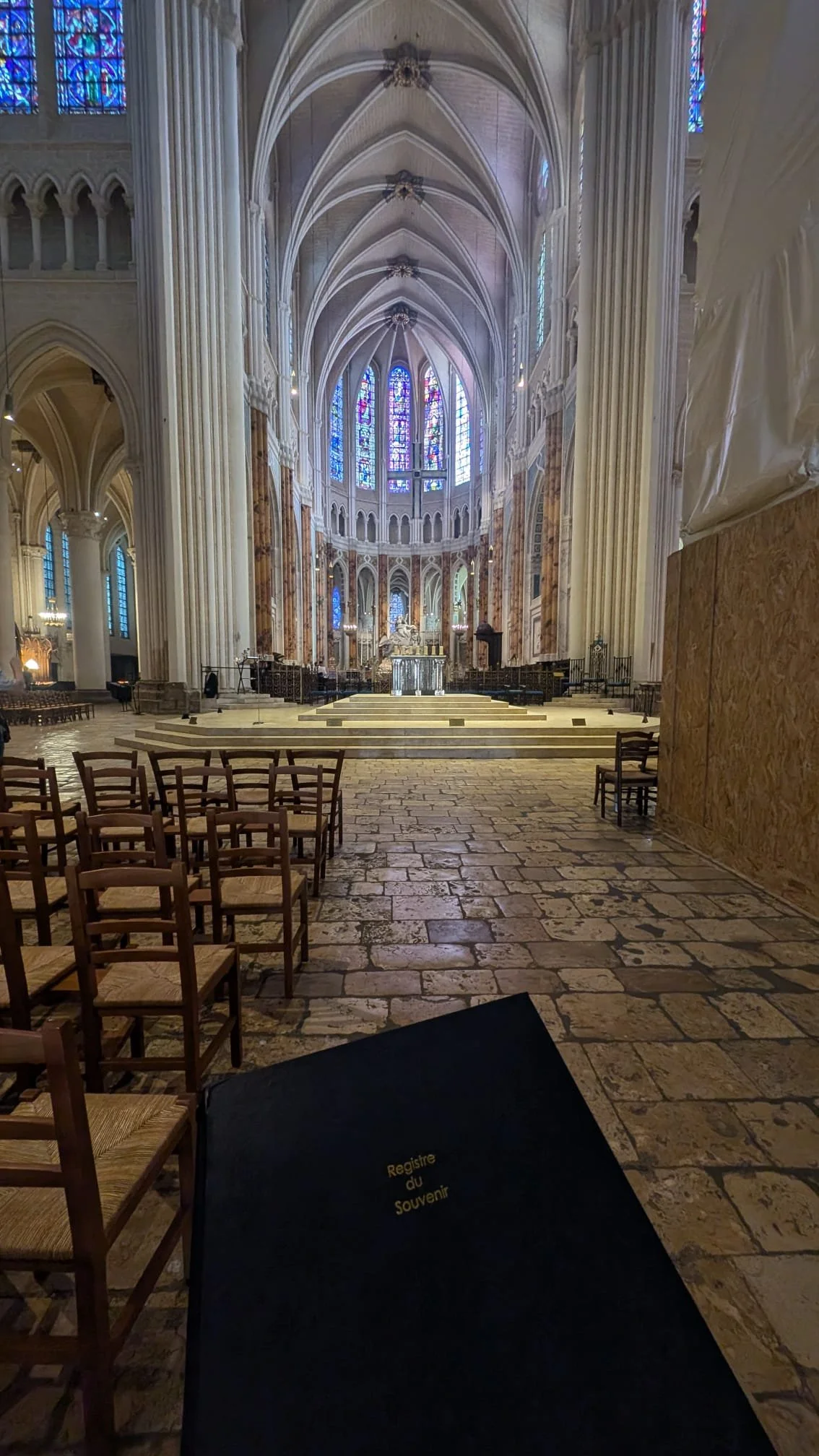 Vue de l'intérieur d'une grande église avec des bancs en bois, des vitraux colorés, une nef haute avec des arches et un autel au fond. On voit aussi un registre de souvenirs sur une table.