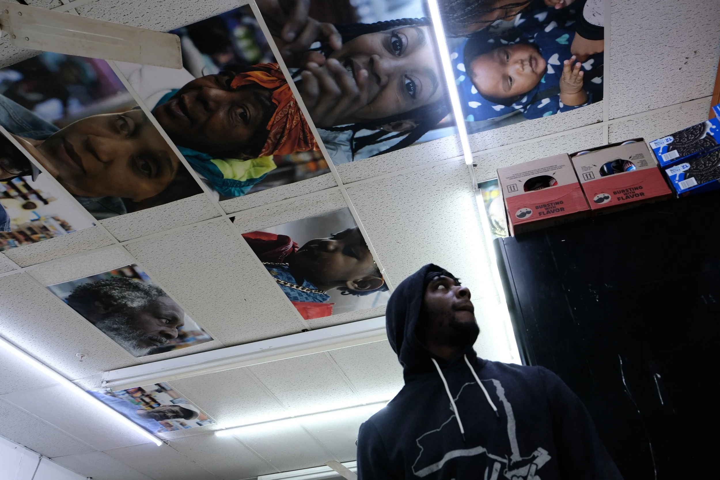  Portraits taken by Kelvin Jackson hang among the ceiling tiles at Ze Mart, with a patron visible at right, on Jan. 10, 2026. Photo by: Micah Orieta 