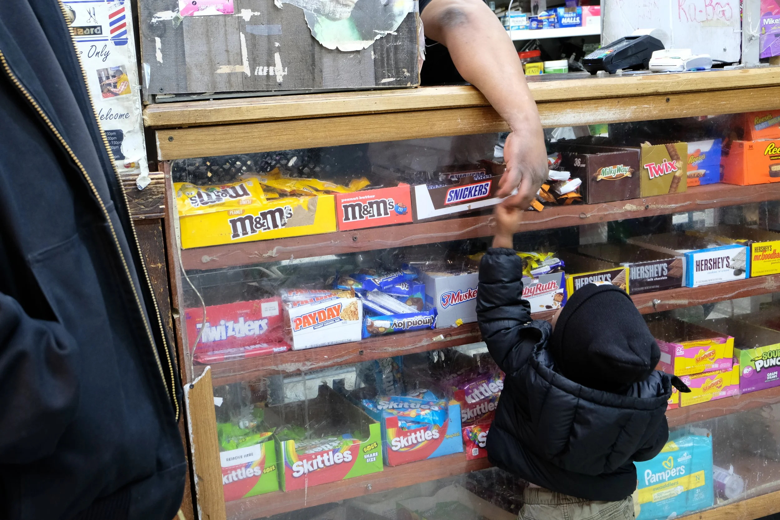  Kelvin Jackson reaches over the counter at Ze Mart to hand candy to a young boy on Jan. 10, 2026. Photo by: Micah Orieta 