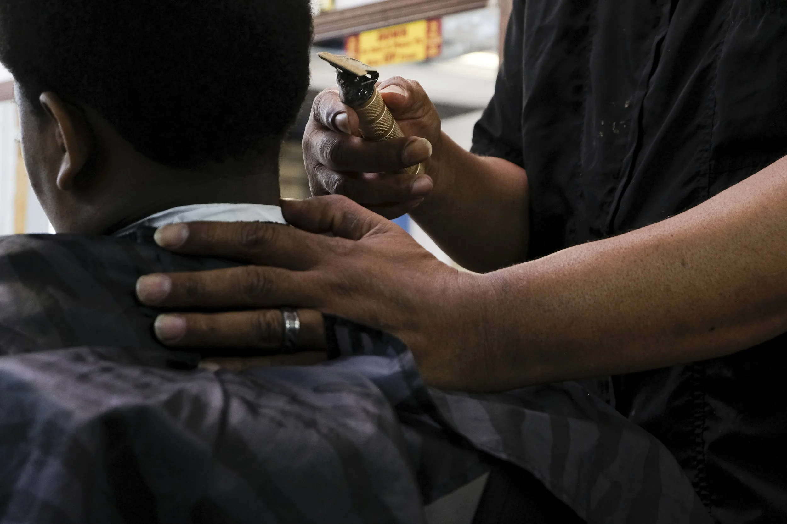 Derrick Franklin's hand rests on the back of a young patron's neck as he holds gold clippers in his other hand at Blue Brothers Barber Shop on South Salina Street in Syracuse, May 16, 2026. Photo by Zahra Perkins. 