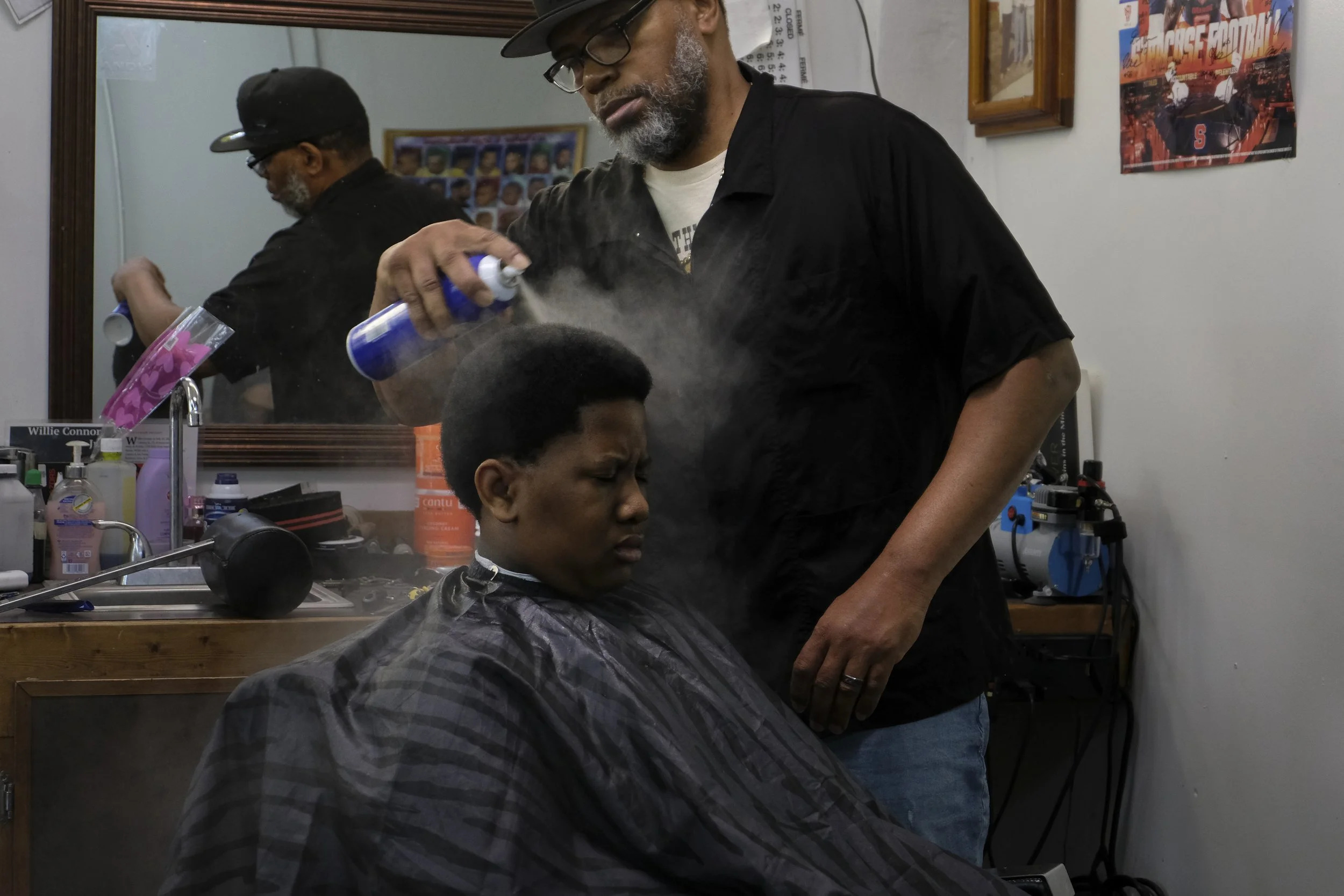  Derrick Franklin applies hairspray to a patron's fresh cut at his station at Blue Brothers Barber Shop on South Salina Street in Syracuse, May 16, 2026. Photo by Zahra Perkins. 