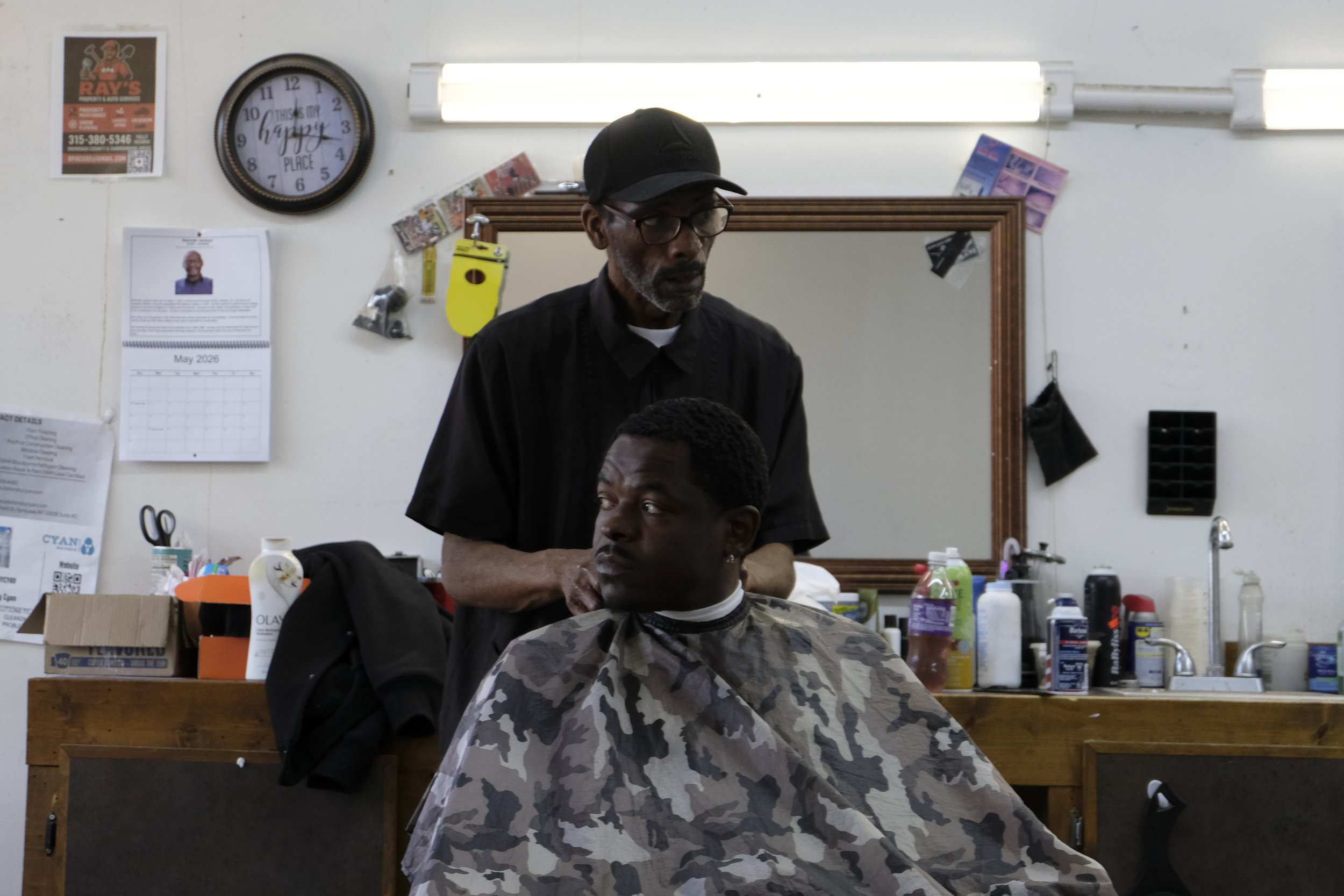  David Blue buttons a cape around a patron seated in his chair at Blue Brothers Barber Shop on South Salina Street in Syracuse, May 16, 2026. Photo by Zahra Perkins. 
