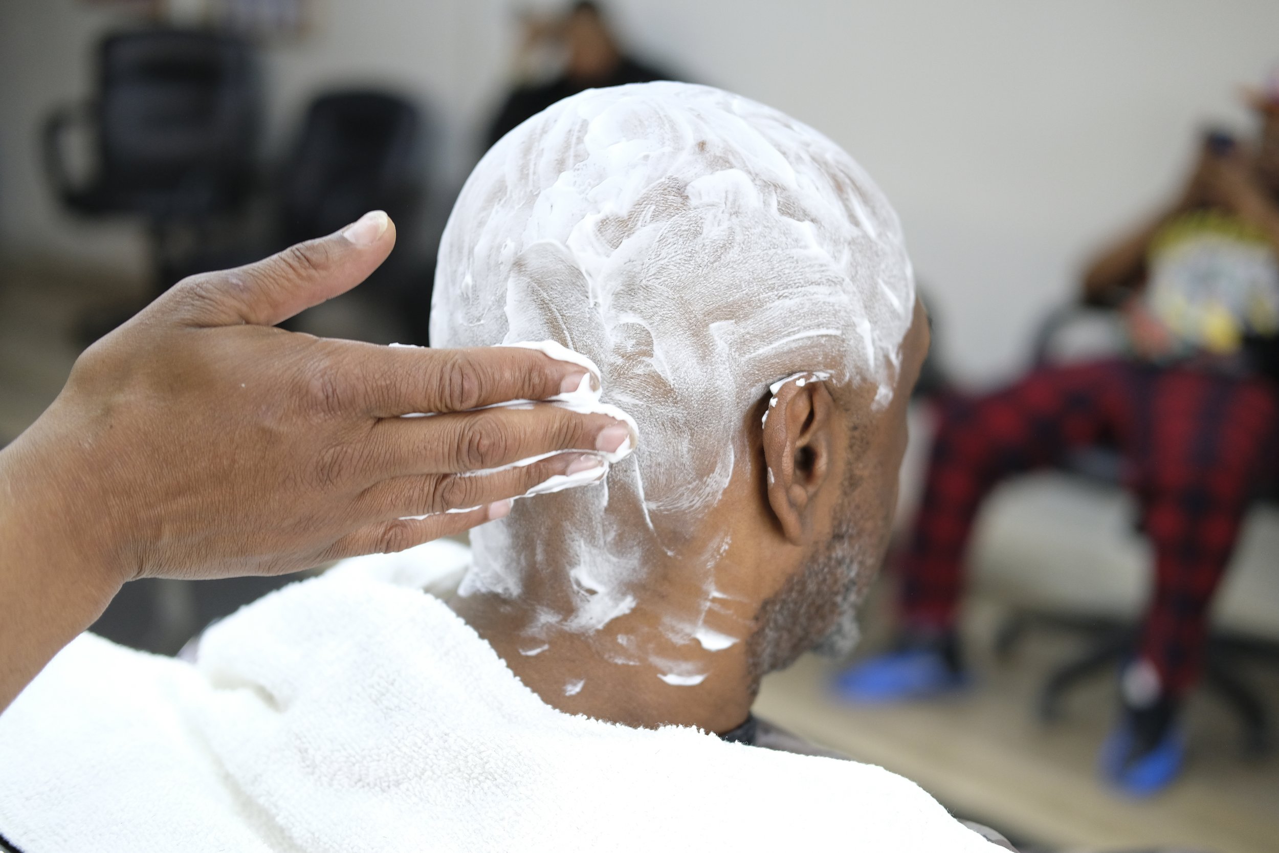  Barber Dexter Bullock rubs shaving cream onto a patron's head as others wait in the background at Blue Brothers Barber Shop on South Salina Street in Syracuse, May 23, 2026. Photo by Manila Southammavong. 