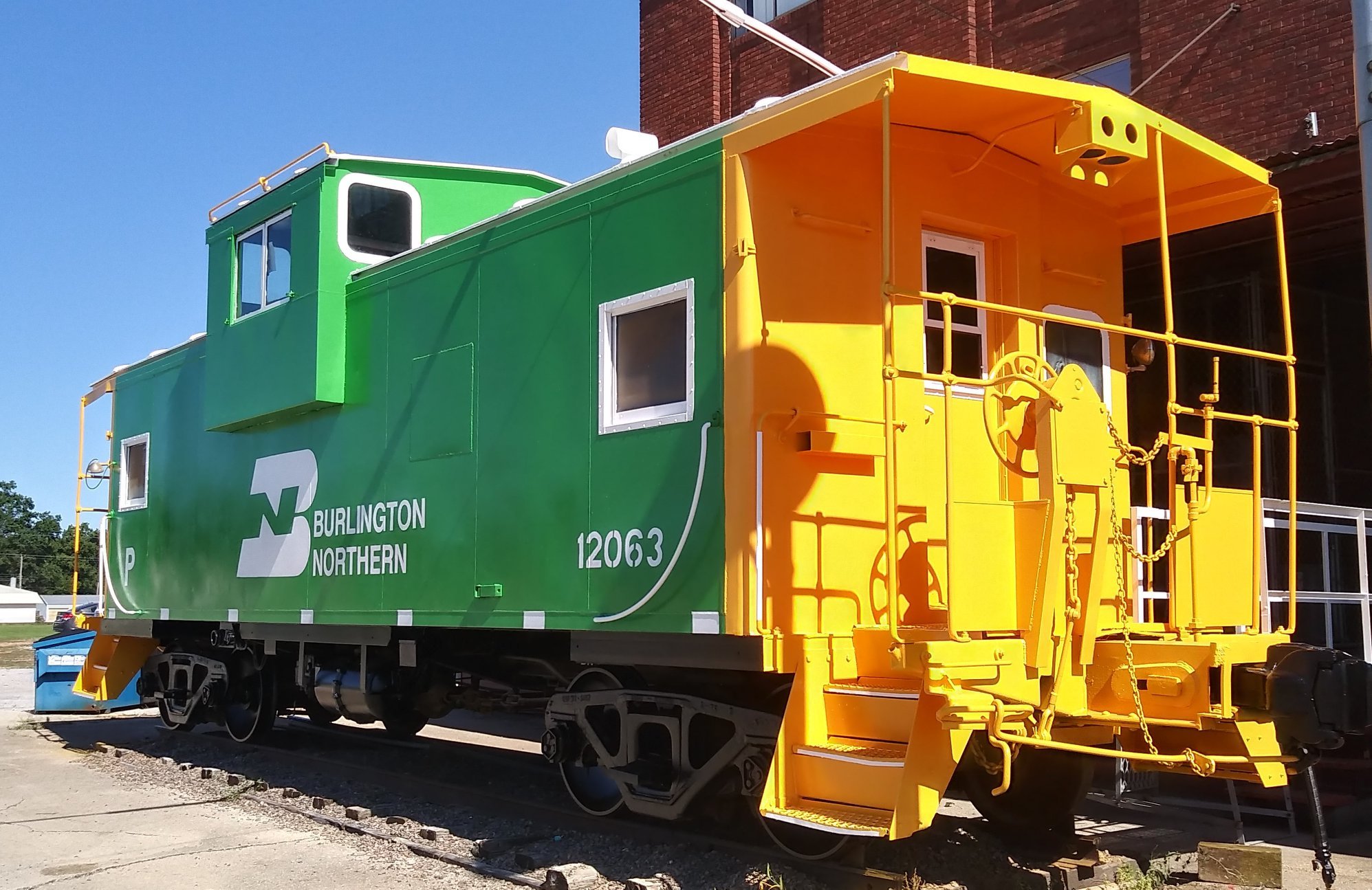 Colorful train car with green and yellow segments, marked with 'Burlington Northern', parked on tracks next to a brick building.
