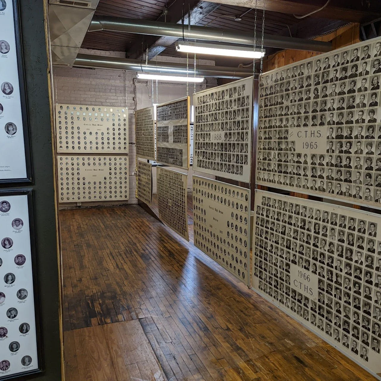 Display of black-and-white portrait photographs of students arranged on large panels in a hallway of a school, with some panels labeled with years and school initials.