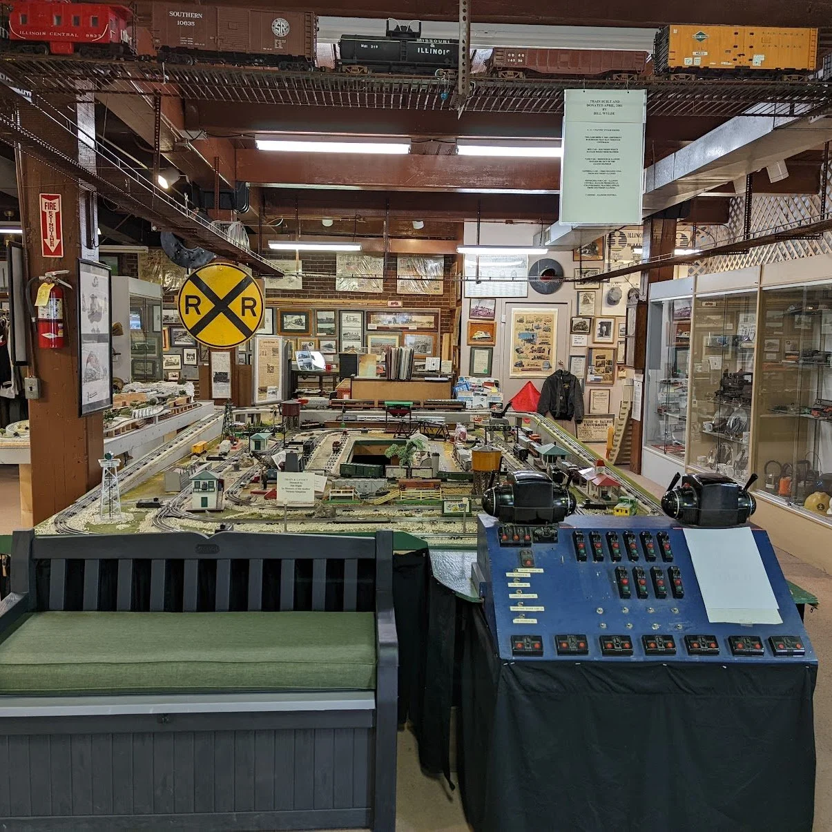 A model train display inside a museum with various model trains on tracks, framed pictures on the wall, and display cases with collectible items.