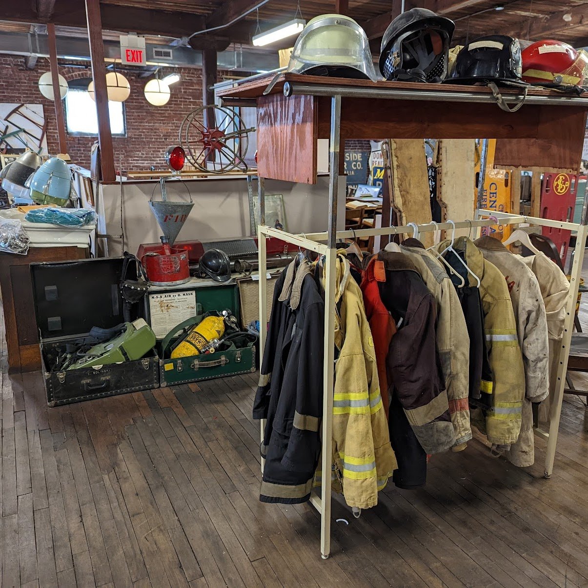 Collection of vintage firefighting gear including jackets, helmets, and equipment in a thrift store.