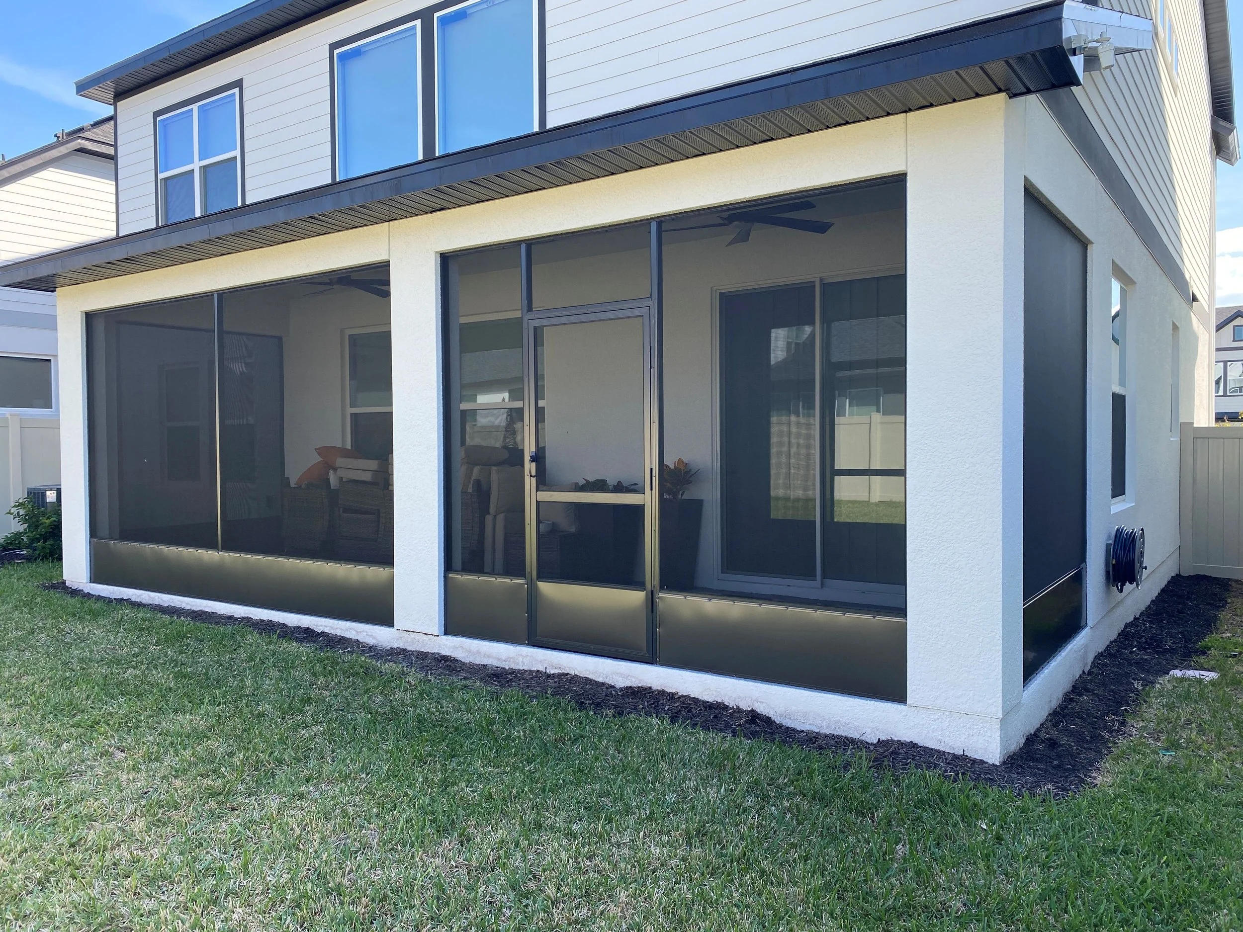 Back view of a two-story house with a screened-in porch area on the ground floor, surrounded by a grassy yard and a white fenced backyard.