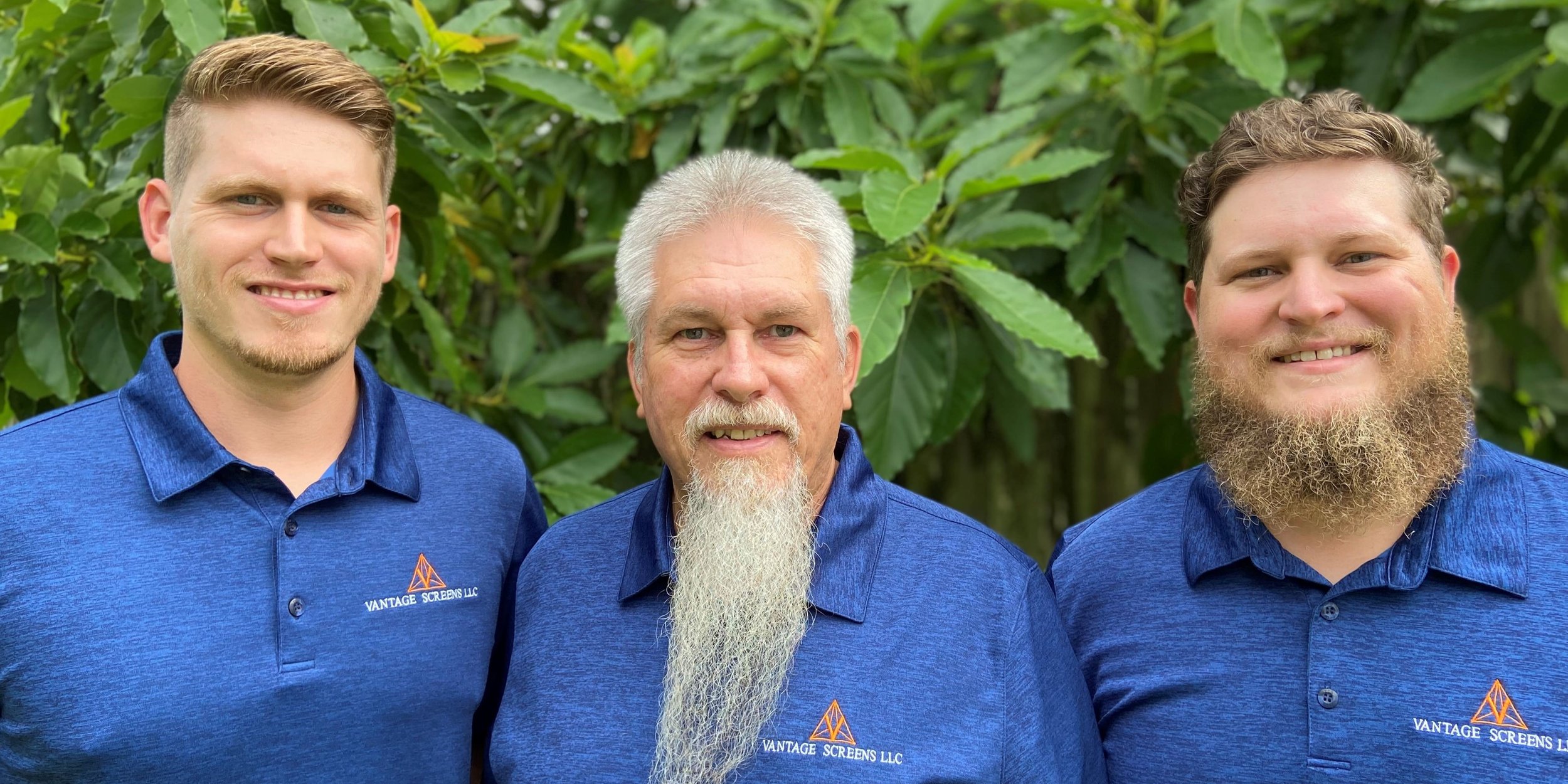 Three men wearing matching blue shirts with the logo 'VANTAGE SCREENS LLC' stand outdoors in front of green foliage, smiling at the camera.