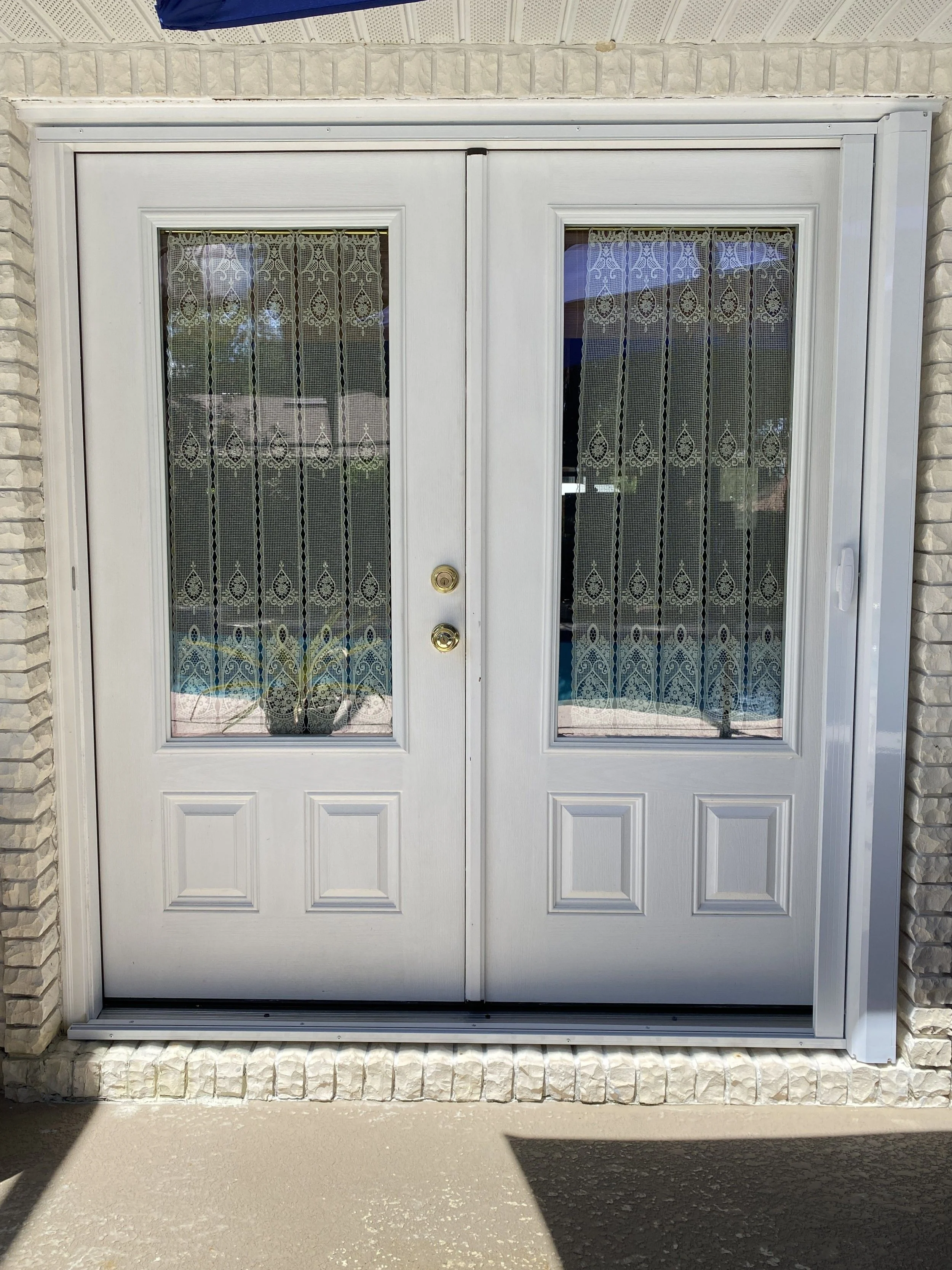 White sliding glass door with lace curtains and brick wall exterior.