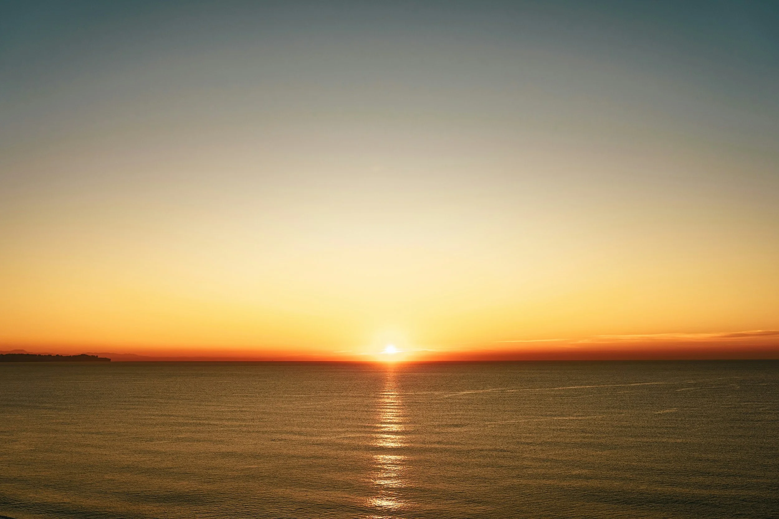Coucher de soleil au-dessus de la mer avec un ciel coloré allant du jaune au bleu, reflet du soleil sur l'eau calme.
